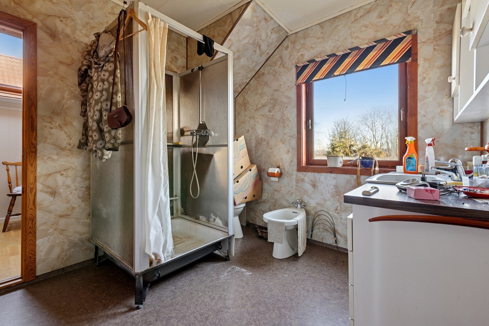 Badet er av eldre dato med baderomsblater, vinlybelegg og innredning med servant, benkeskap, blandebatteri og speilt samt toalett og dusjkabinett. Galleribilde