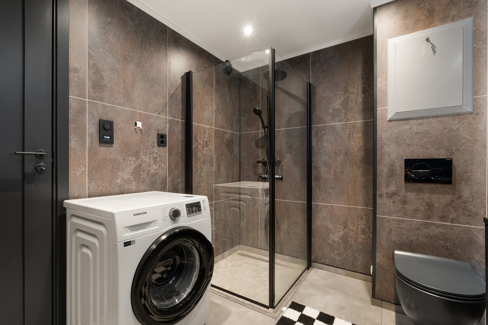 Dusjhjørne med glassdører, tropedusj, vegghengt toalett og opplegg til vaskemaskin. Galleribilde