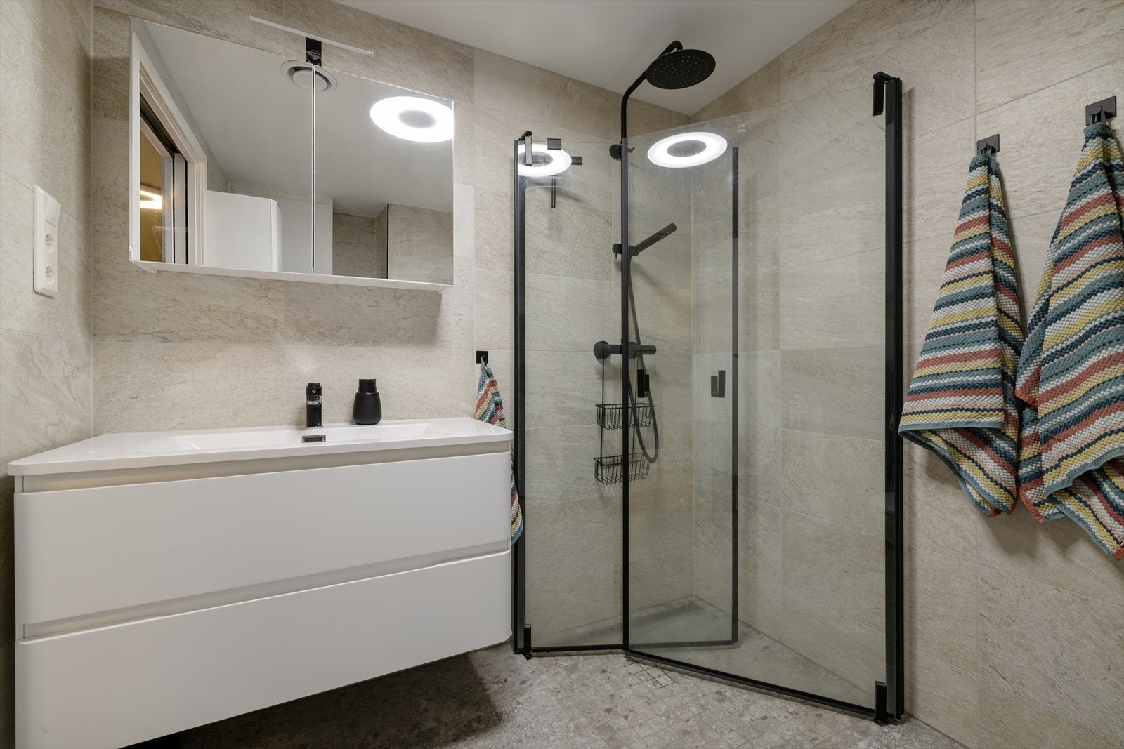 Moderne og delikat baderomsinnredning med glatte fronter, nedsenket servant og innfellbare dusjvegger kombinert med stilrent, sort dusjtilbehør. Galleribilde