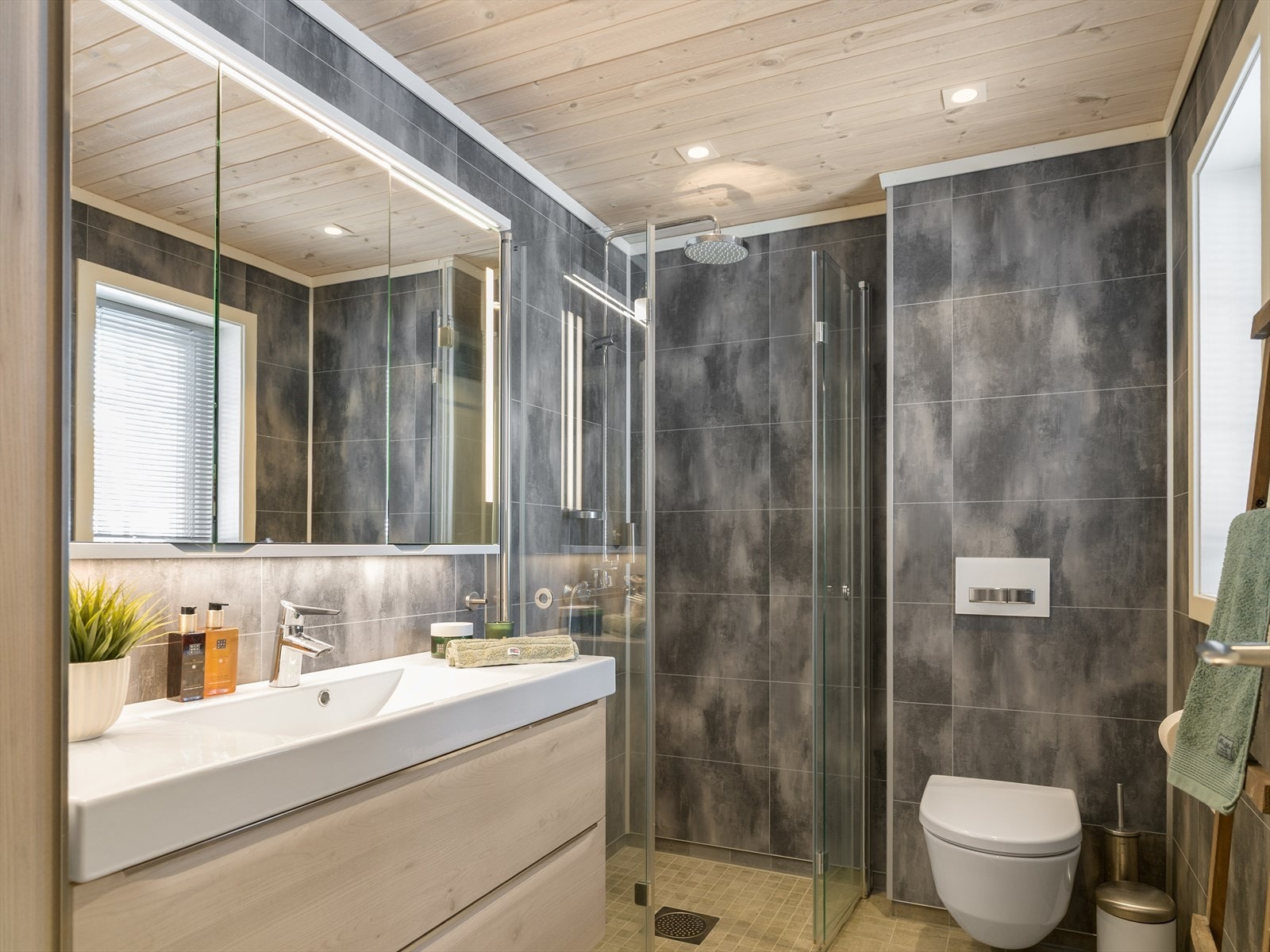 Pent- og praktisk baderom med dusjhjørne, vegghengt WC, flisgulv med varme. Panel i himling med innfelte downlights. Galleribilde