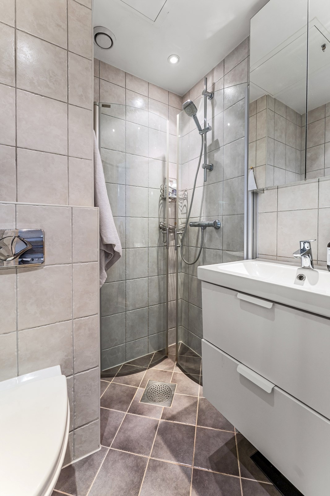 Dusjhjørne med dører i herdet glass, heldekkende servant med underskuffer, speilskap over servant og vegghengt toalett. Galleribilde