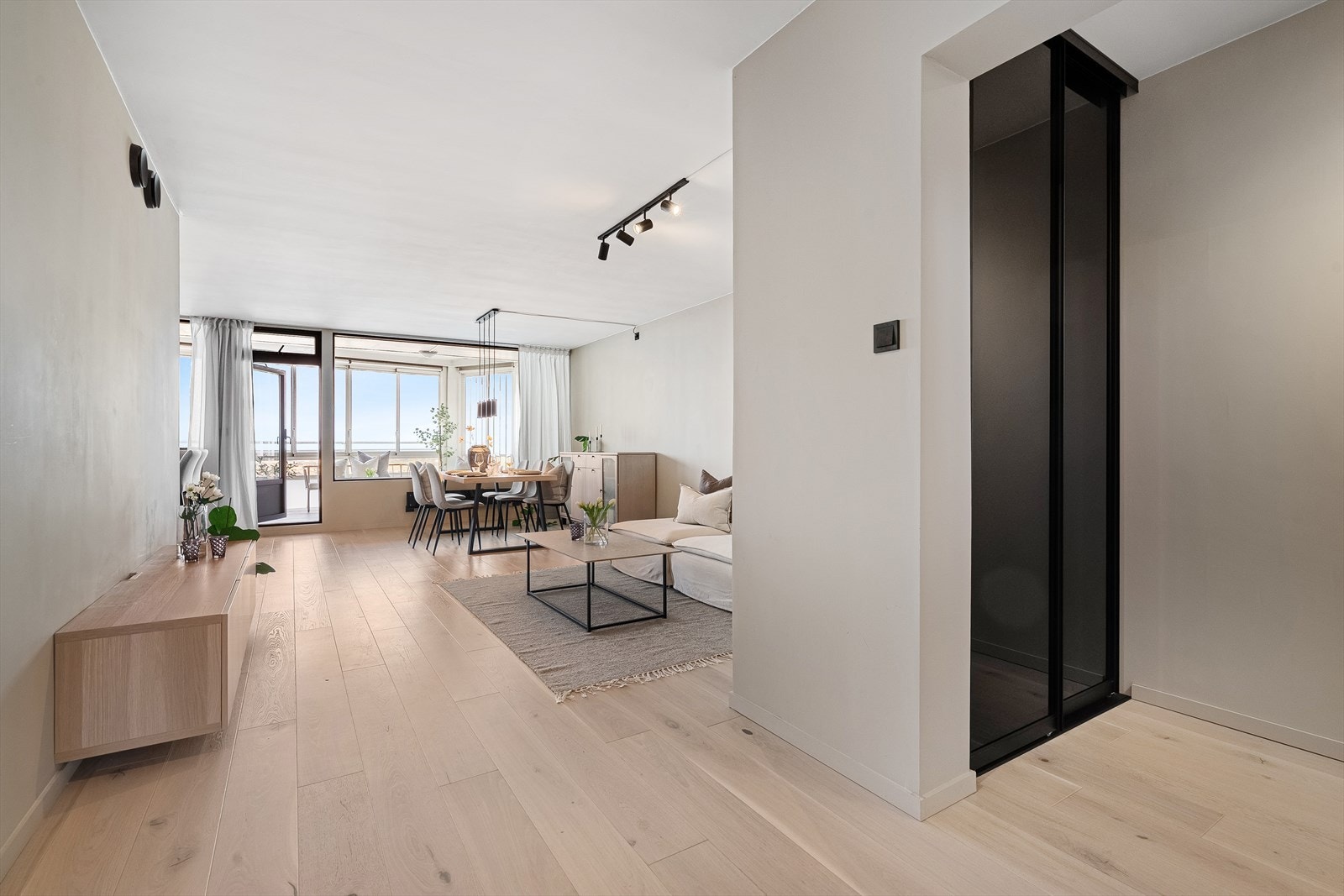 Boligen har gjennomgående en-stavs gulv med lyse lister i samme farge som veggene, kombinert med svarte stikkontakter og brytere som glir sømløst inn i interiøret. Galleribilde