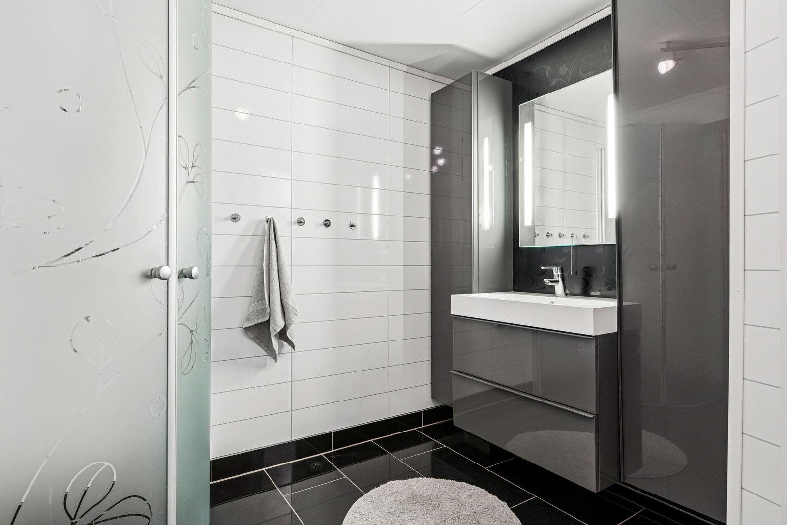 Innredningen består av vegghengt servantinnredning, speil med sidelys, vegghengte høyskap og dusjhjørne med dører. Galleribilde