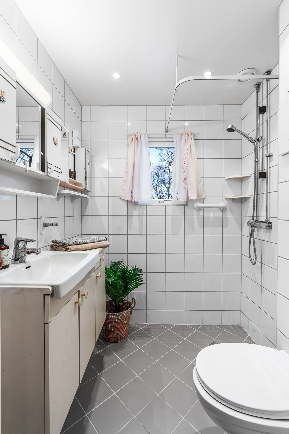 Rommet har et dusjhjørne med forheng, veggmontert toalett og opplegg for vaskemaskin Galleribilde