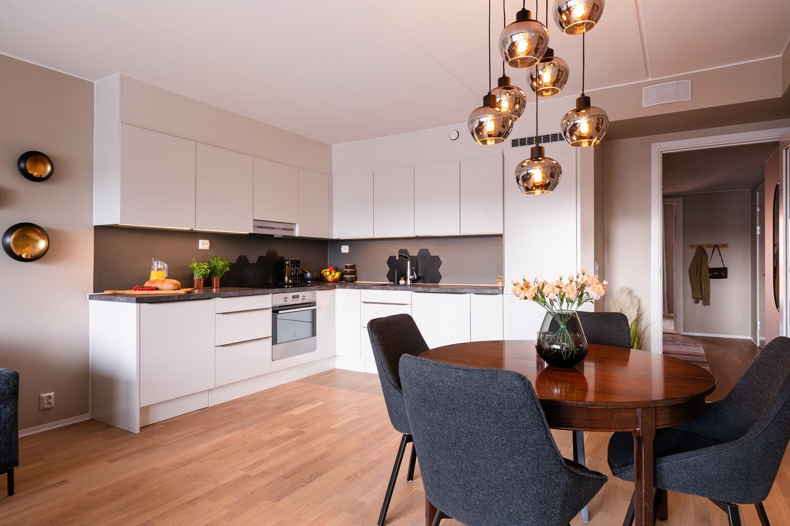 Moderne kjøkken fra HTH med lyse, glatte fronter og laminat benkeplate med nedfelt vaskekum. Kjøkkenet har integrert kjøleskap, oppvaskmaskin, induksjonstopp og stekeovn, samt ventilator over kokeplass. Det er også montert vannstoppsystem og komfyrvakt. Galleribilde