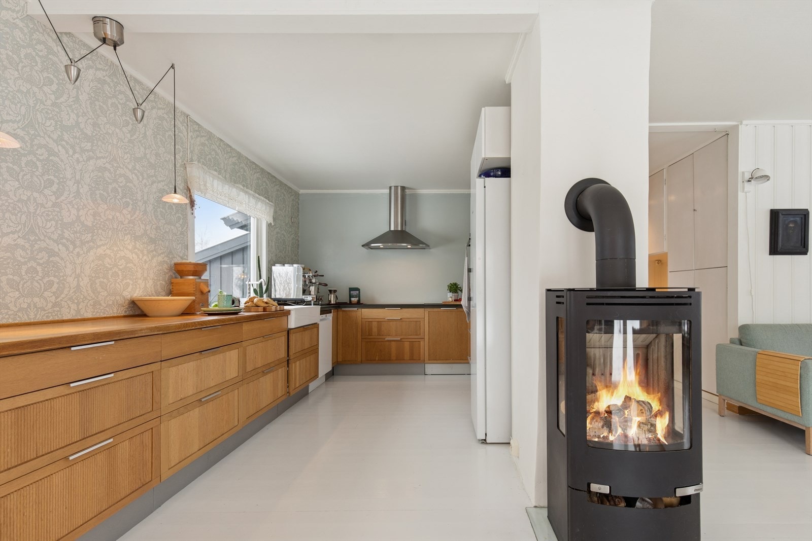 Stemningsskapende vedovn skaper varme og hygge på kjølige dager, og fungerer som et naturlig midtpunkt mellom stue og kjøkken. Galleribilde