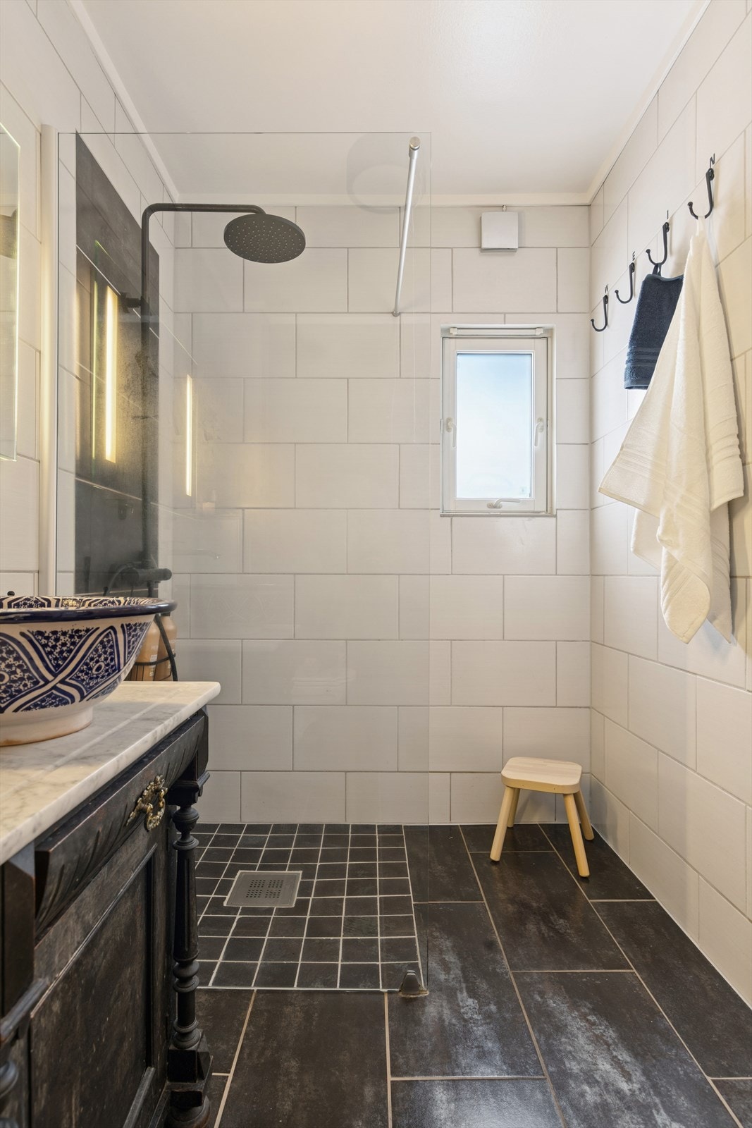 Servantskap med ovenpåliggende servantbolle, vegghengt speil med integrert belysning, dusjhjørne med glassvegg og vegghengt toalett. Galleribilde