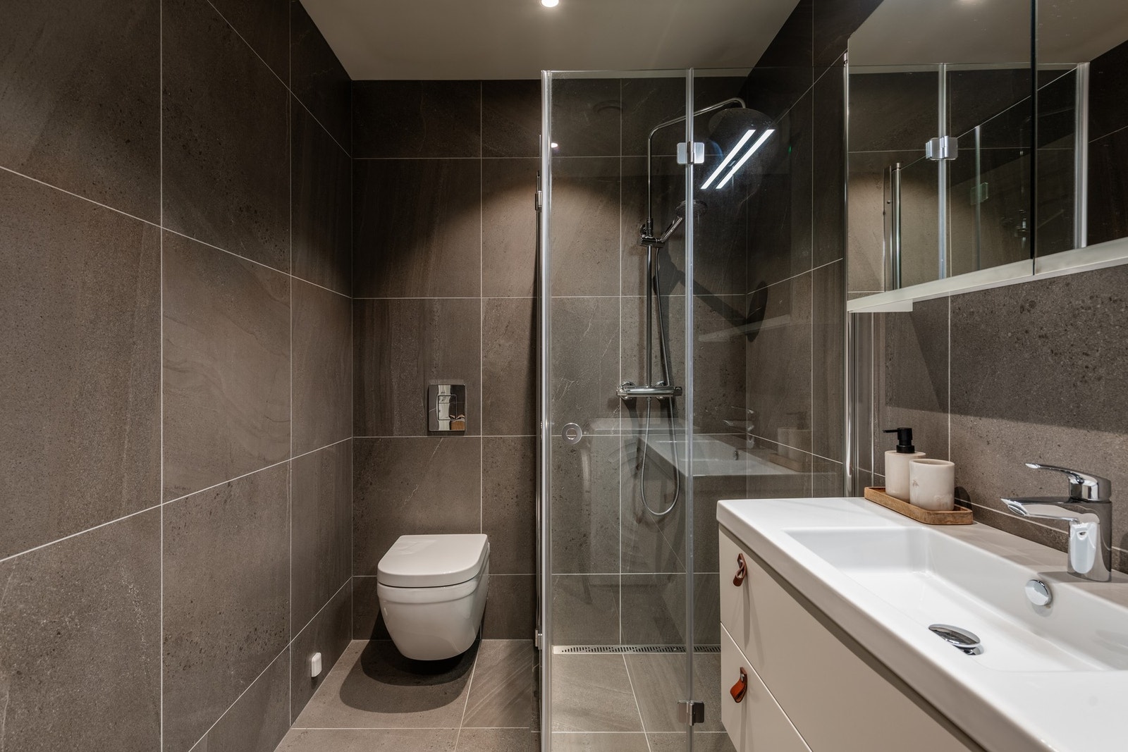 Lekkert bad med servantinnredning, veggheng toalett og dusj med glassdører, samt opplegg for vaskemaskin. Galleribilde