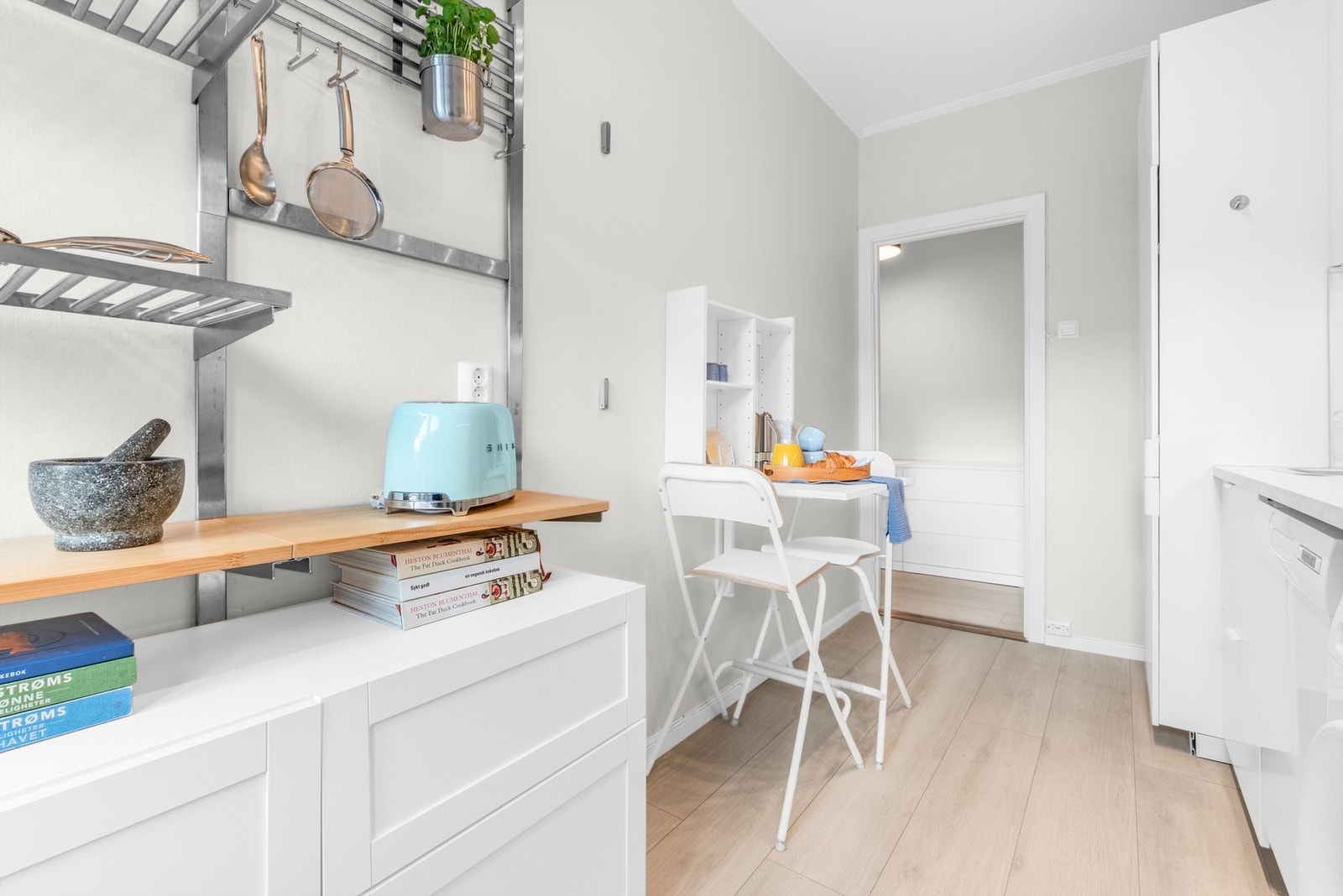 Kjøkkenet er lyst og stilrent, med praktiske hylleløsninger i tillegg til mye oppbevaring i skapene Galleribilde