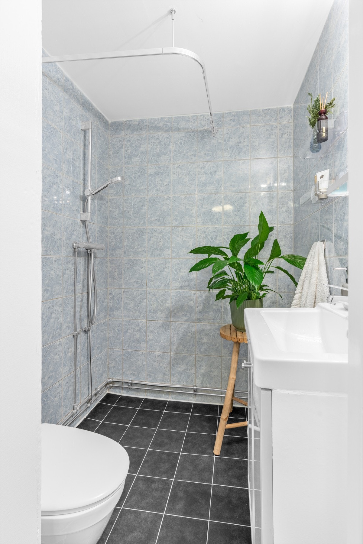 Badet har mørke gulvfliser, kombinert med lyseblå veggfliser og en hvitmalt kontrastvegg Galleribilde