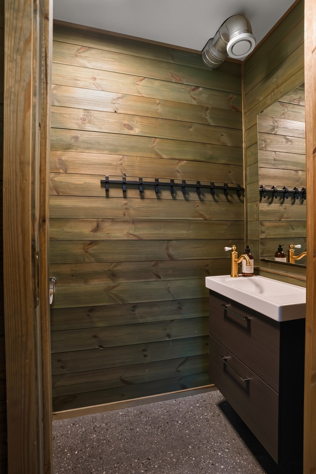 Praktisk toalettrom med klosett og servant med innredning. Vegger og himling er belagt med panel, og gulvet i slipt betong med vannbåren varme gir et tøft og moderne uttrykk. Galleribilde