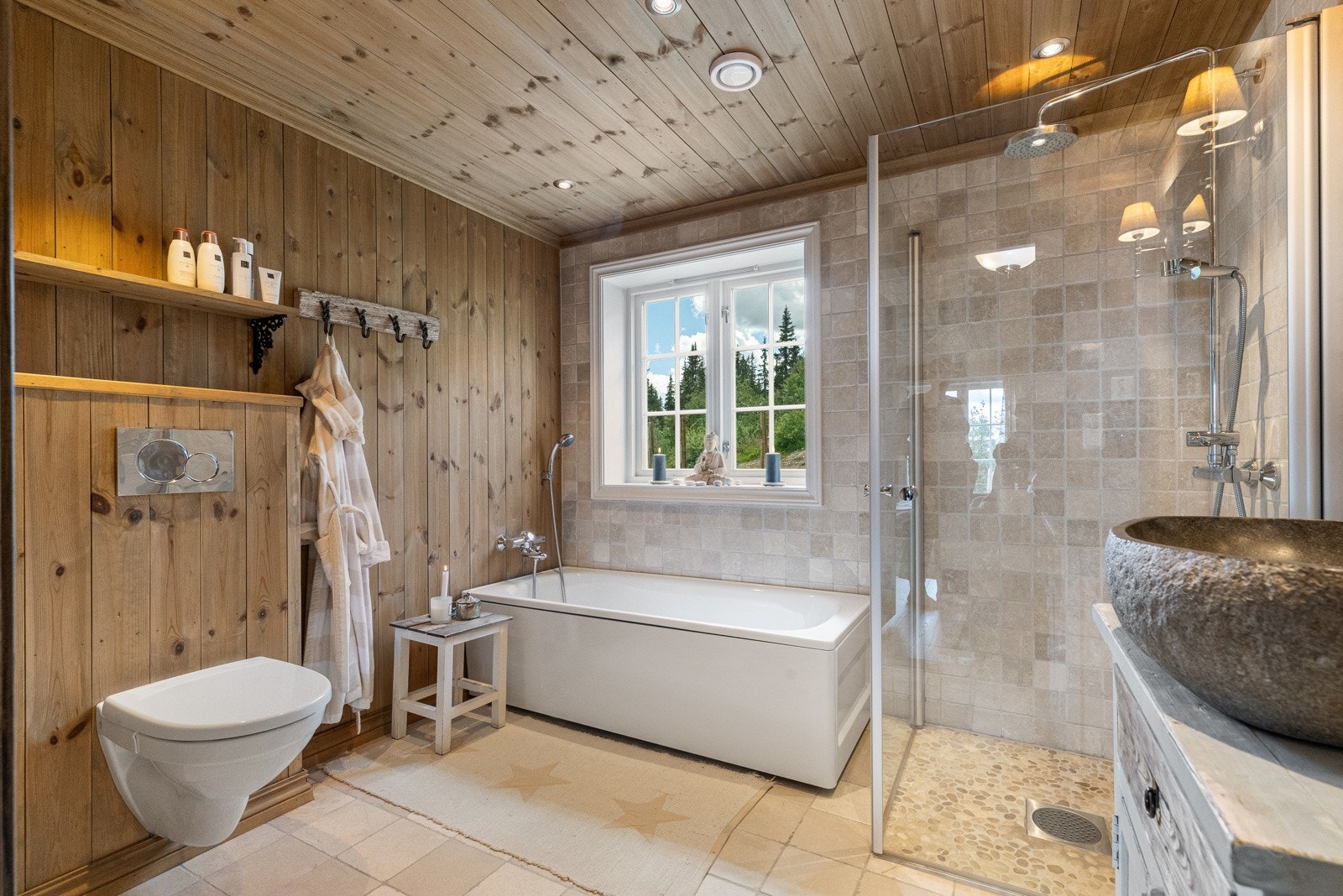 Badet i første etasje har en lun stil. Flislagt gulv og på veggen i dusjnisje og forbi vinduet hvor badekaret står Galleribilde