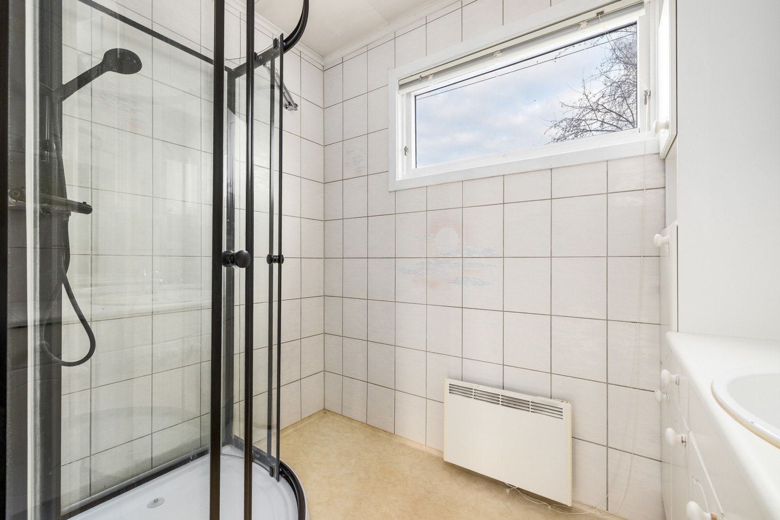 Delikat baderom med dusjhjørne i glass, lyse fliser og vindu som gir godt dagslys. Galleribilde