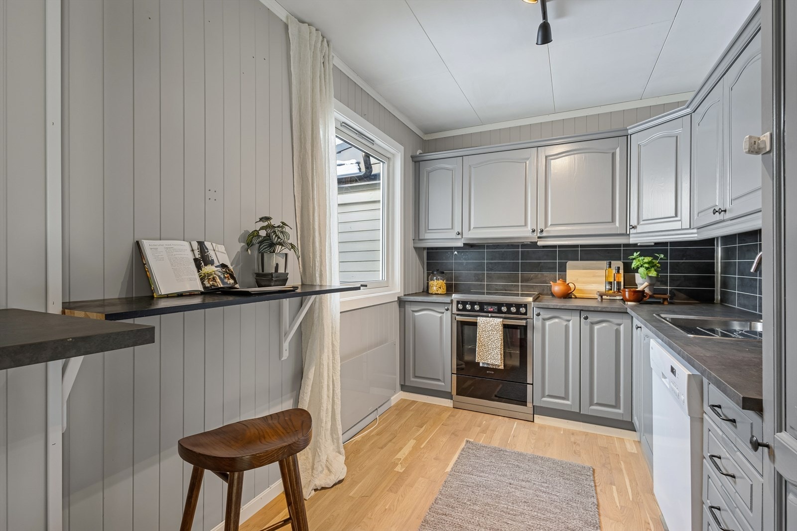 Kjøkkenet er innredet med gråmalte, profilerte fronter og grå benkeplate i laminat. Et romslig kjøkken hvor man har godt med skap- og skuffeplass, samt gode arbeidsflater på benk. Galleribilde