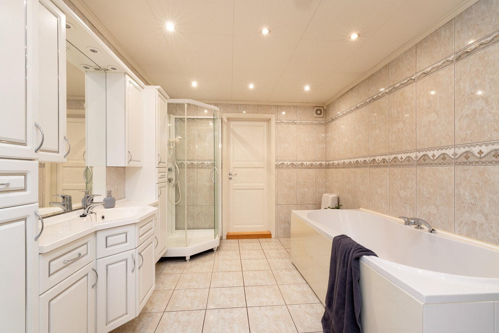 Baderommet er flislagt med varme i gulv og inneholder servant med oppbevaring, dusjkabinett, badekar og toalett. Galleribilde