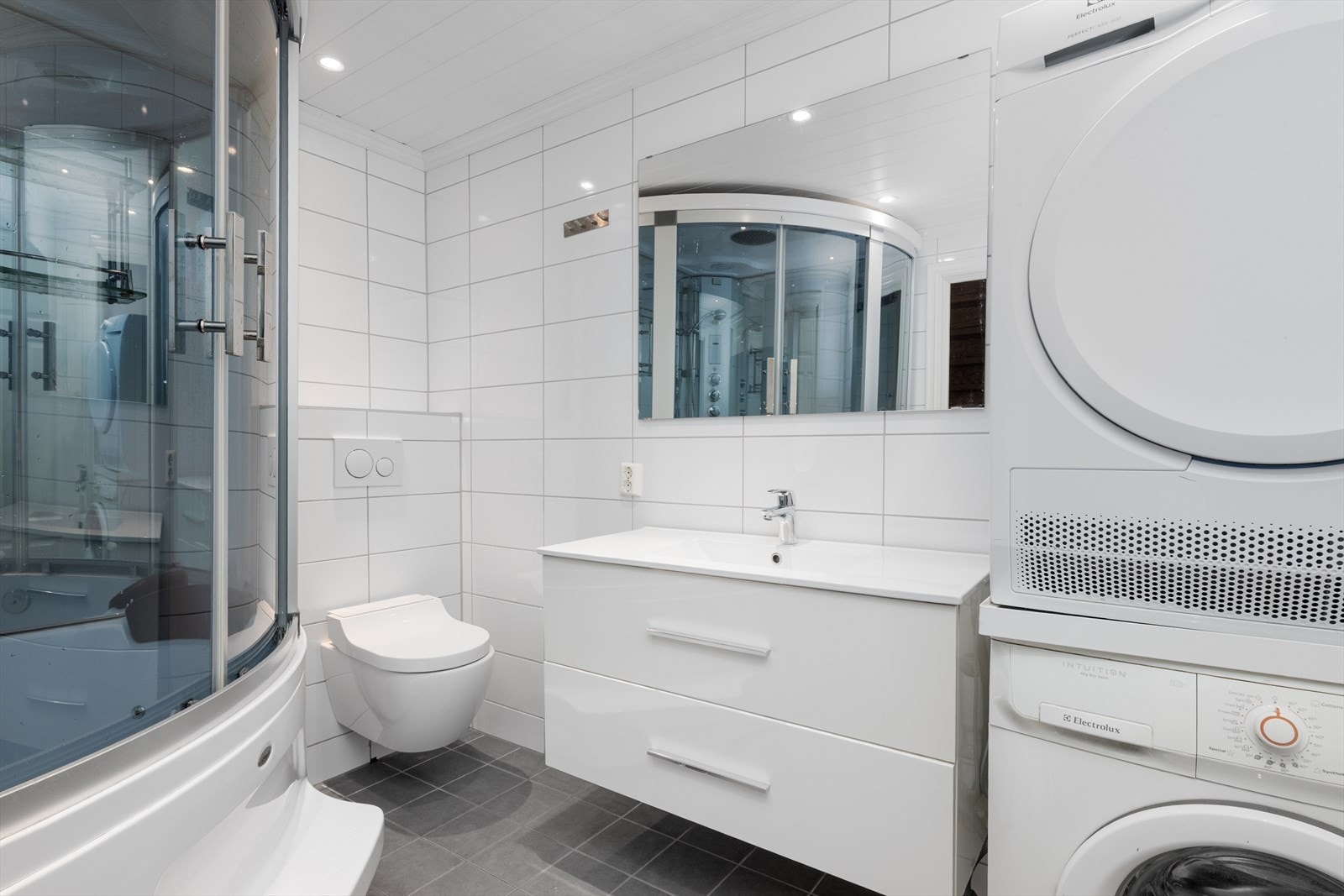 Badet i 1. etasje inneholder heldekkende servant med underskap, speil med lys, vegghengt dusjtoalett, dusjkabinett/badekar og opplegg til vaskemaskin. Galleribilde