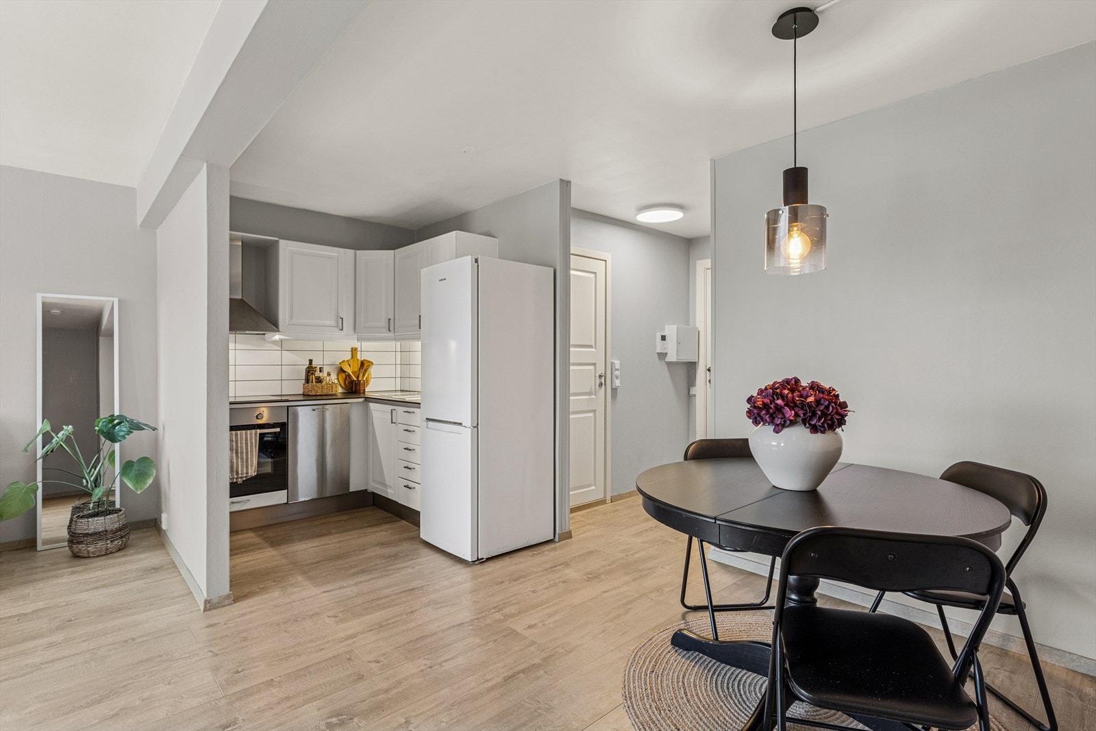 Kjøkkenet har en innredning med hvite, profilerte fronter og en laminatbenkeplate med planlimt kum i rustfritt stål. Galleribilde