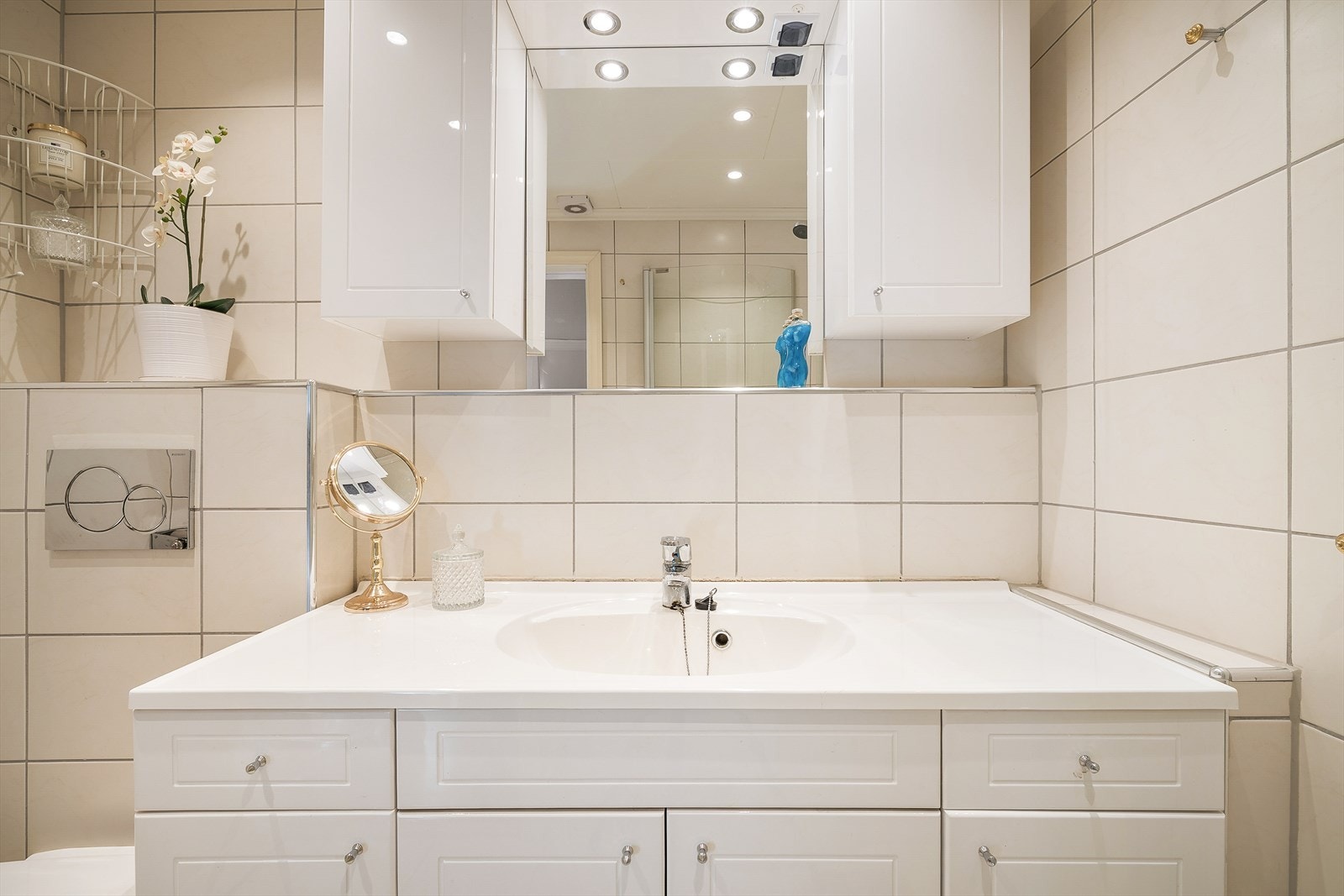 Rommet er innredet med vask med underskap og skuffer, overskap og speil på vegg, dusjhjørne med foldedører og vegghengt toalett. Galleribilde