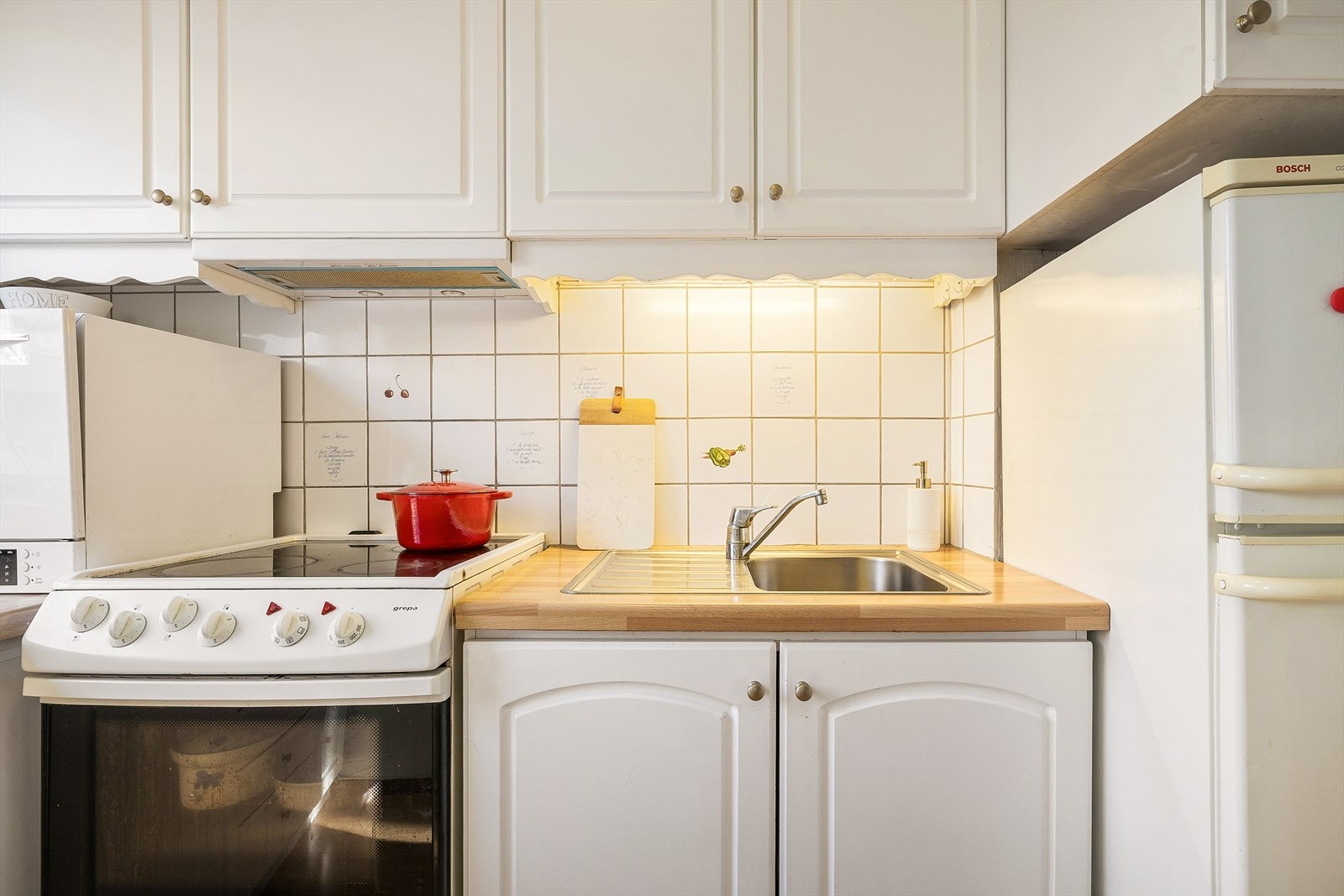 Innredet med laminat benkeplater med nedfelt stål vaskebeslag, benkeopvaskmaskin, frittstående komfyr og kombiskap. Galleribilde