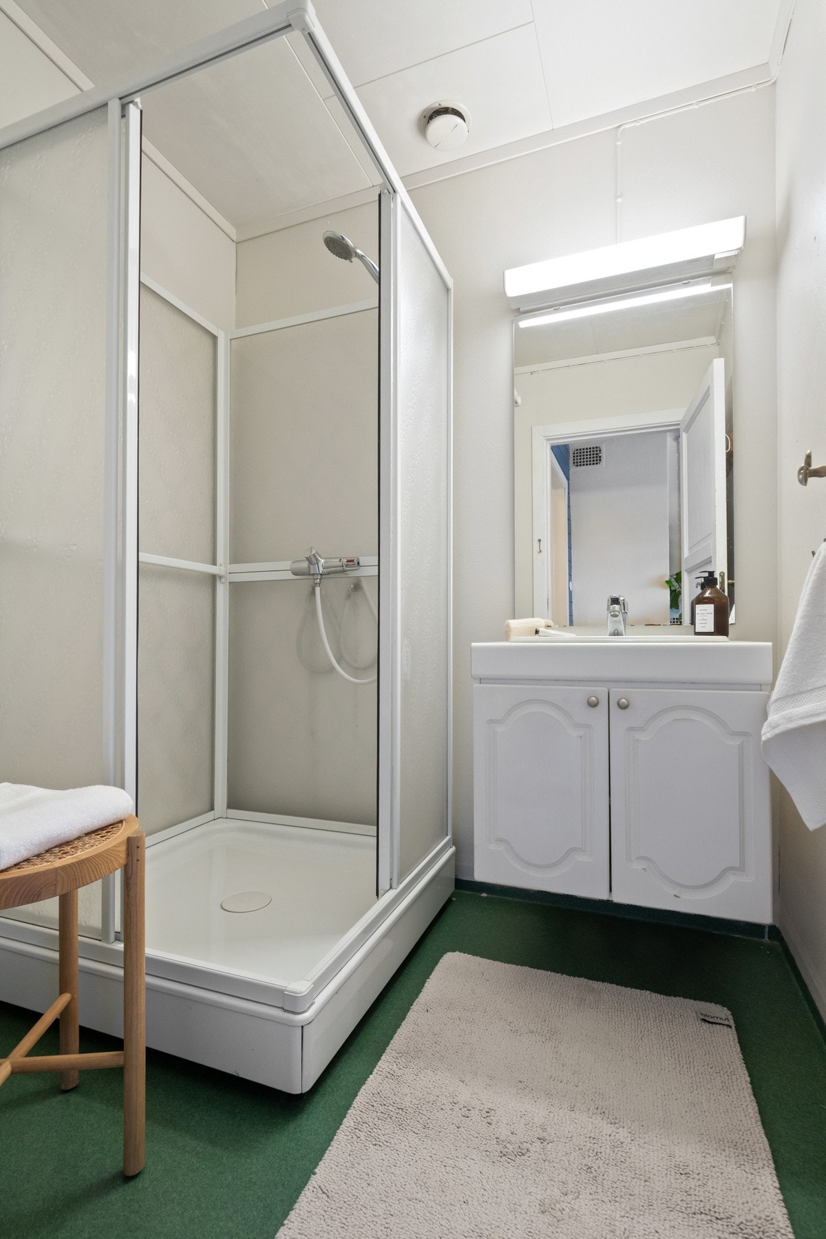 Rommet har dusjkabinett, malte vegger og vinylbelegg på gulv. Her er det servant med hvite underskap og speil med belysning. Galleribilde