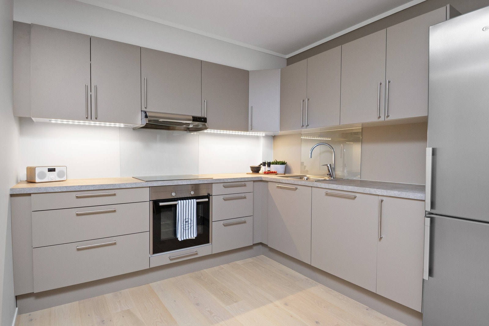 Kjøkkenet fremstår som stilrent og moderne, oppført i en funksjonell L-form som gir god arbeidsflyt og rikelig med skap- og benkeplass. Galleribilde