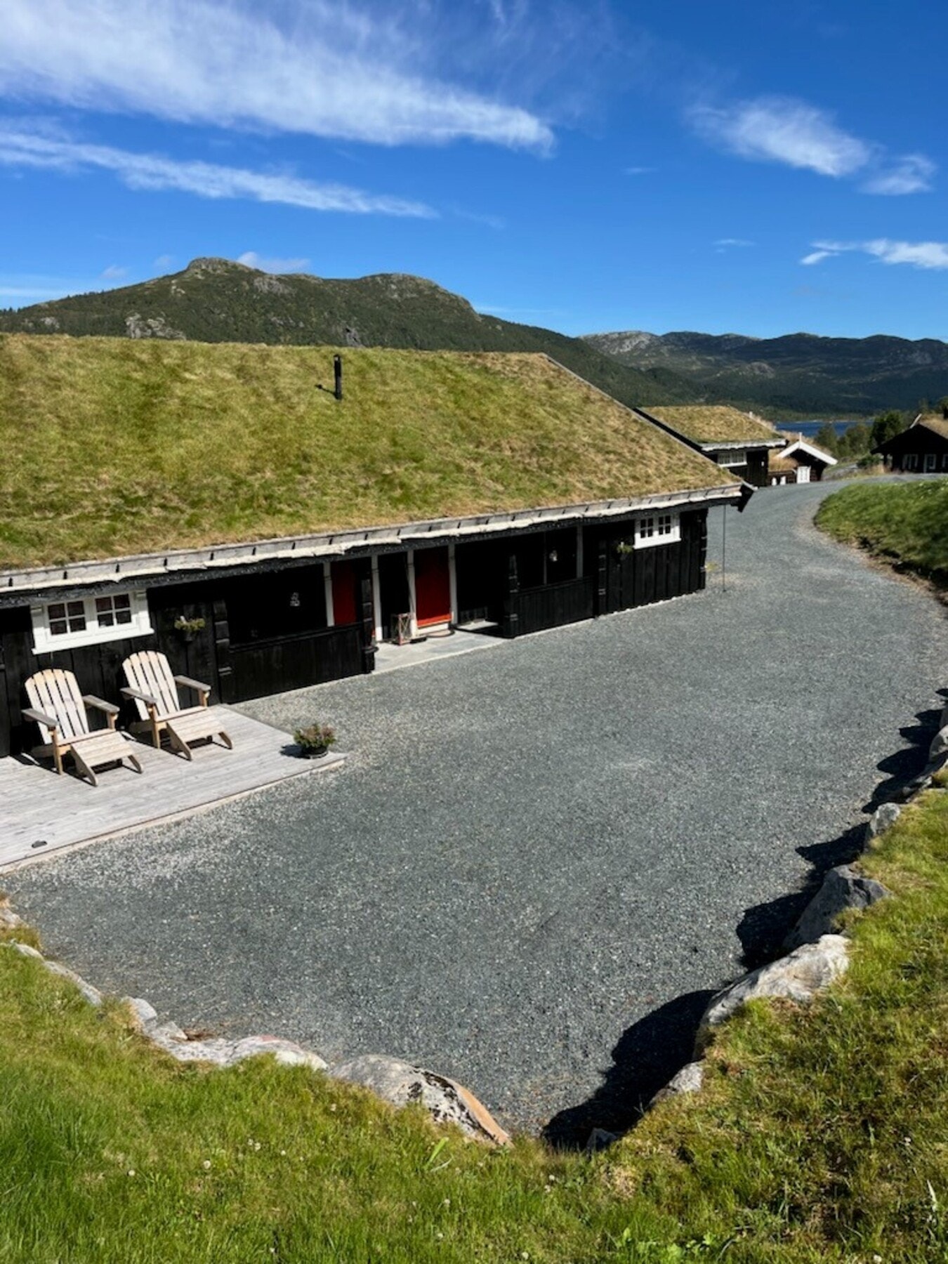 Fra eiendommen på sommerstid. Tomta er svært pent opparbeidet med plen, natursteinsmur og gruset tun (selgers bilde) Galleribilde