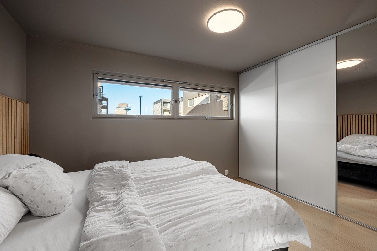 Romslig soverom malt i lune, behagelige fargetoner, med stor skyvedørsgarderobe som gir gode oppbevaringsmuligheter og lystette plisségardiner for optimal komfort og skjerming. Galleribilde