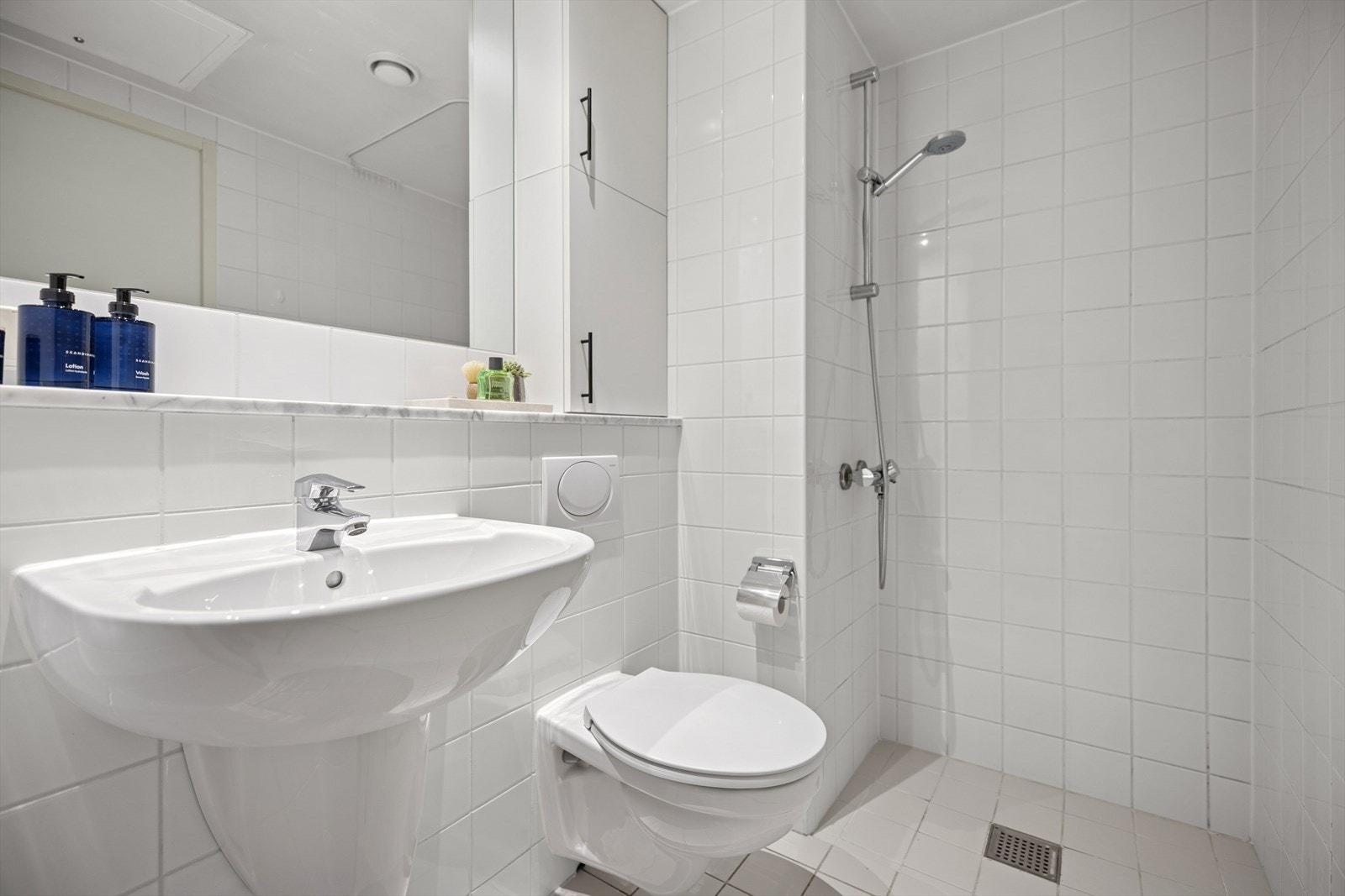 Badet er innredet med veggfestet klosett, servant med speil og integrert hylleplass. Galleribilde