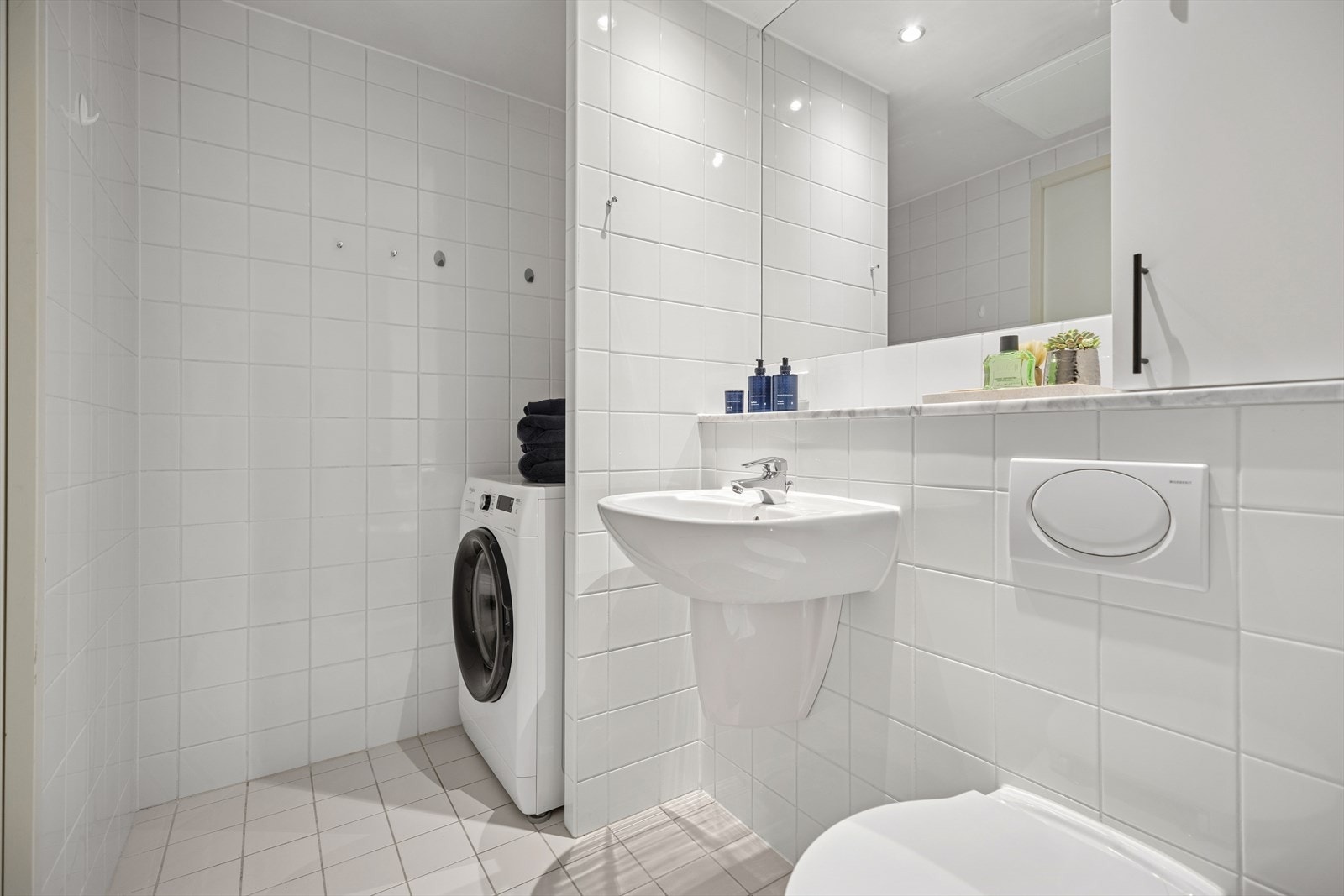 Romslig og lyst bad med flislagte vegger og gulv. Praktisk nisje med opplegg for vaskemaskin og plass til tørketrommel. Galleribilde