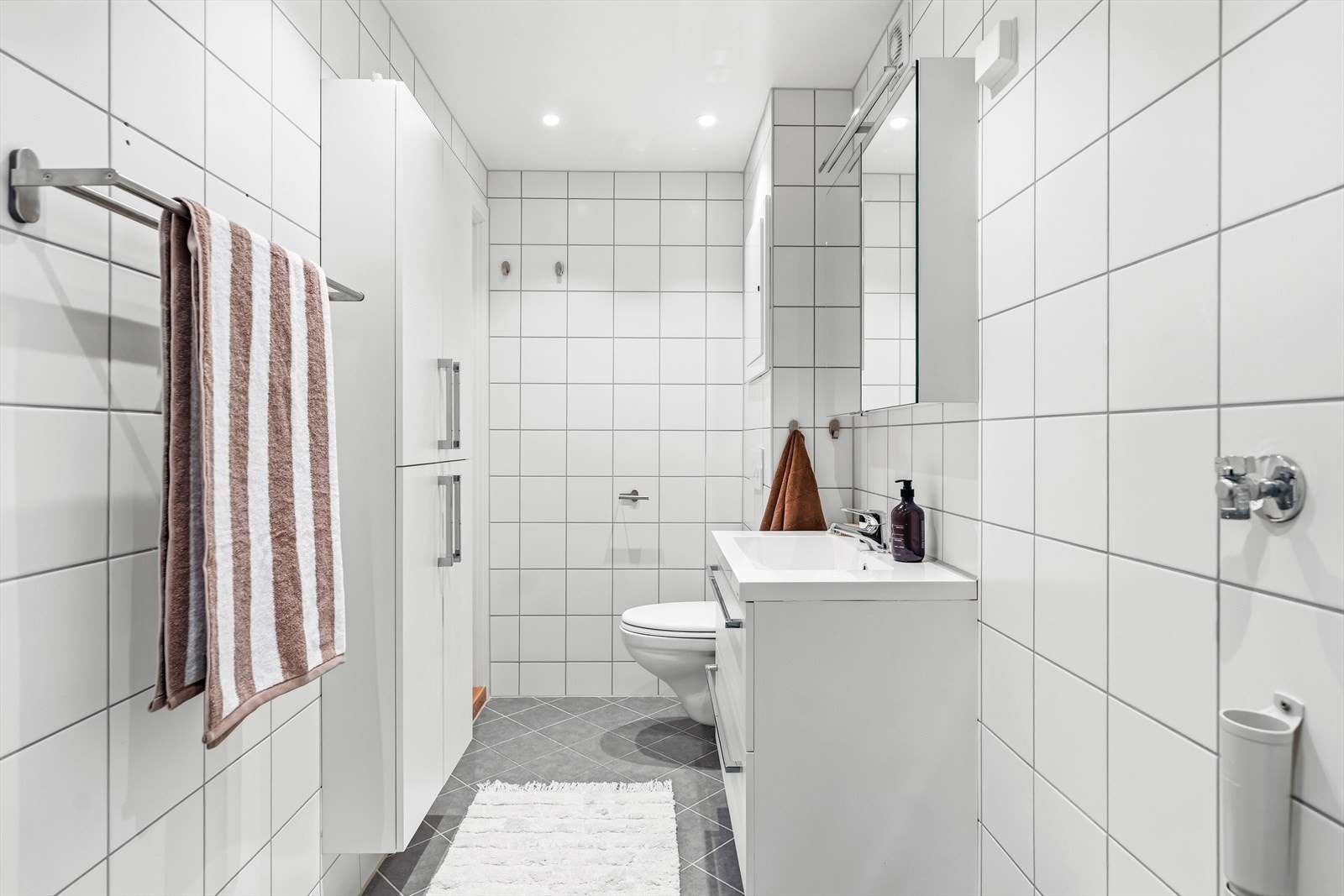 Det er grå fliser på gulv, hvite fliser på vegger, downlights og gulvvarme. Opplegg for vaskemaskin. Galleribilde