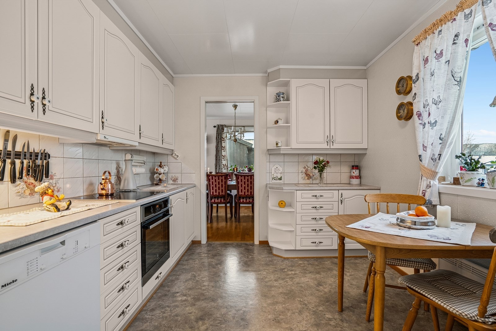 Kjøkkenet har en tidløs innredning med lyse profilerte fronter, laminert benkeplate mede nedfelt kjøkkenvask og fliser på vegg over benk Galleribilde