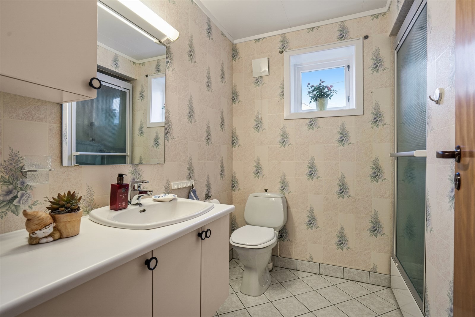 Badet er fra byggeår med flislagt gulv og vegger mede våtromsvinyl - Her finner du toalett, dusjkabinett og baderomsinnredning Galleribilde