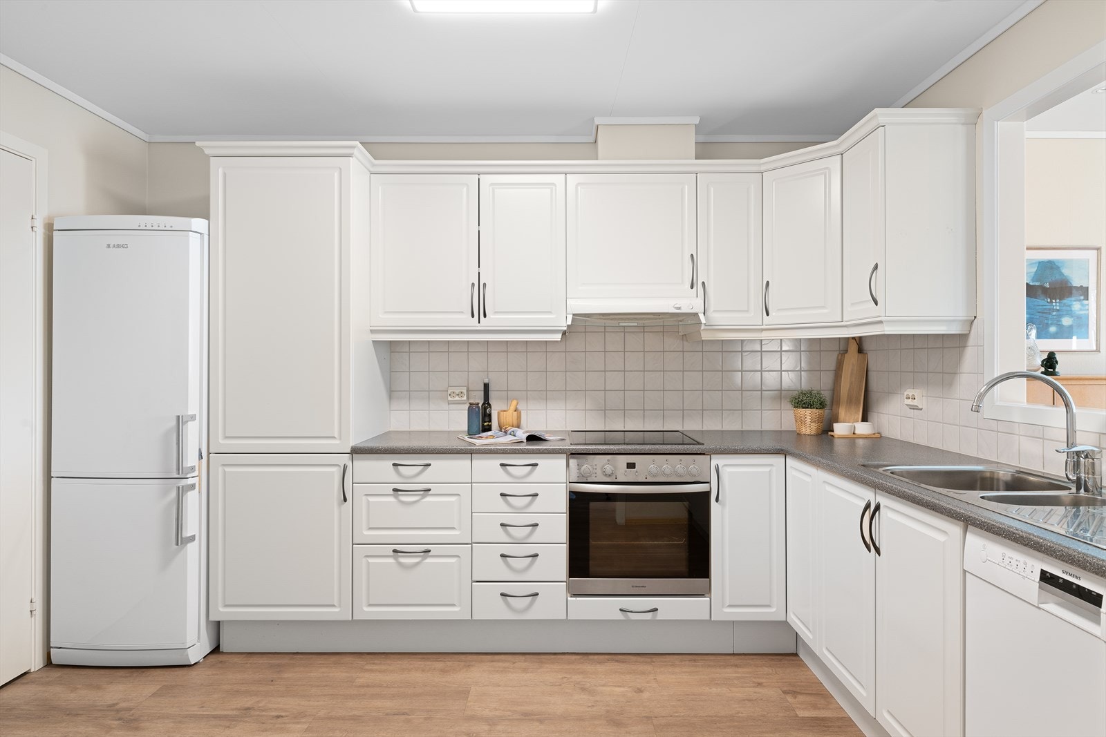 Klassisk innredning med hvite, profilerte fronter og fliser over benk. Det er lagt opp til god arbeidsflyt, med integrert stekeovn og platetopp. Galleribilde