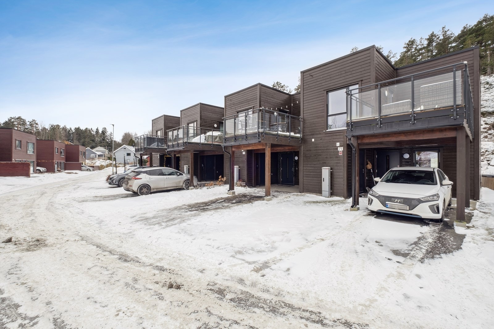 Asfaltert inngangsparti med parkering i carport som har el-bil lader montert. Galleribilde