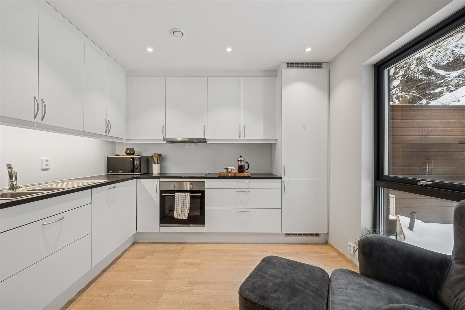 Aubo kjlkkeninnnredning med hvite, glatte fronter og en laminat benkeplate med planlimt kum i rustfritt stål. Galleribilde