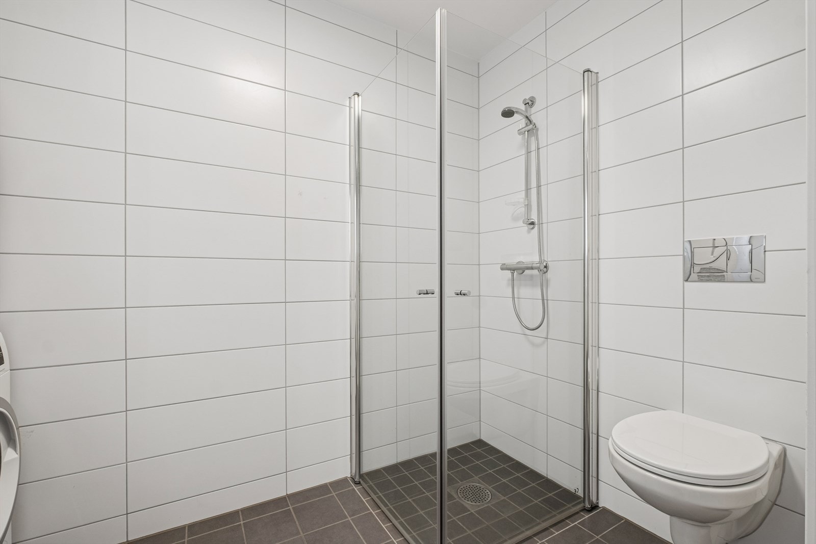 Badet er utstyrt med vegghengt toalett, dusjhjørne med glassvegger, samt baderomsinnredning med servant, blandebatteri og speil. Galleribilde