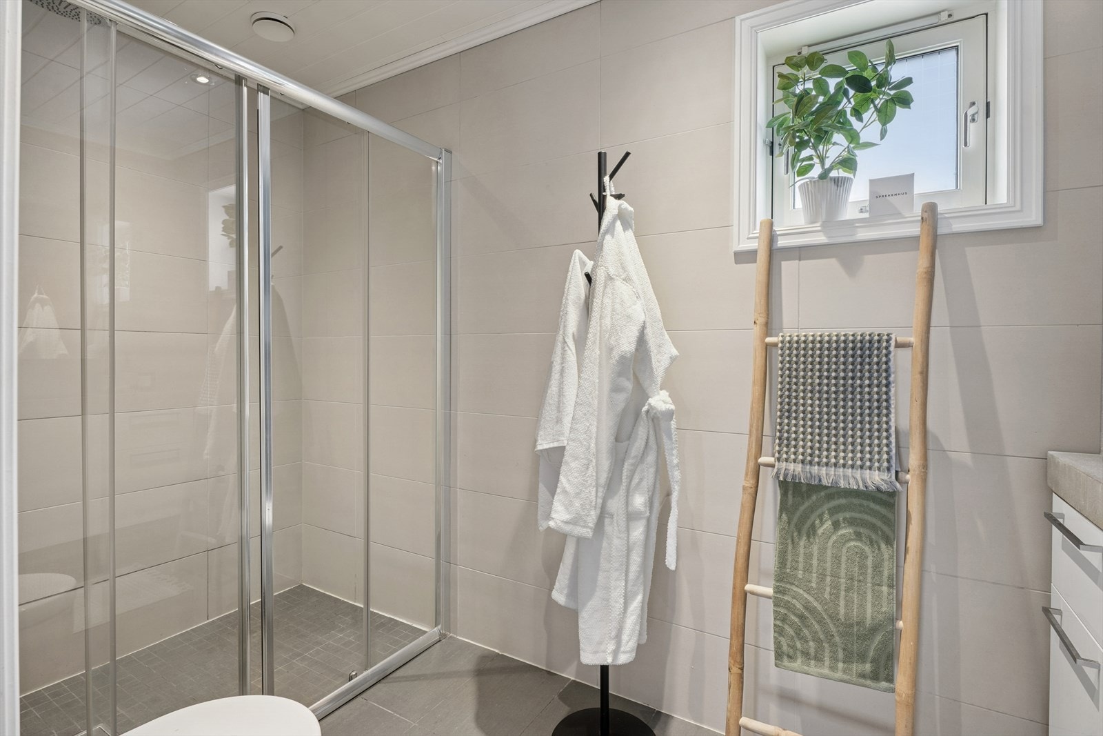 Veggene har elegante, lyse fliser, mens gulvet er belagt med mørkere grå fliser med elektriske varmekabler, som gir både komfort og et moderne uttrykk Galleribilde