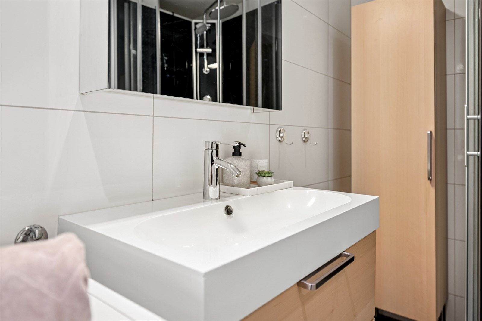 Badet er innredet med en baderomsinnredning med nedfelt servant, veggmontert toalett , dusjkabinett og opplegg for vaskemaskin. Galleribilde