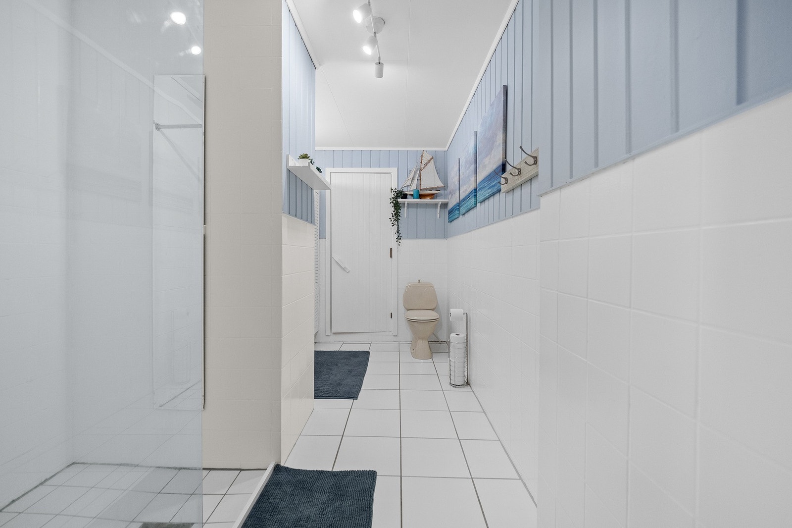 Baderom med lyse fliser og en dusjnisje. Vegghyller gir ekstra oppbevaringsplass. Galleribilde