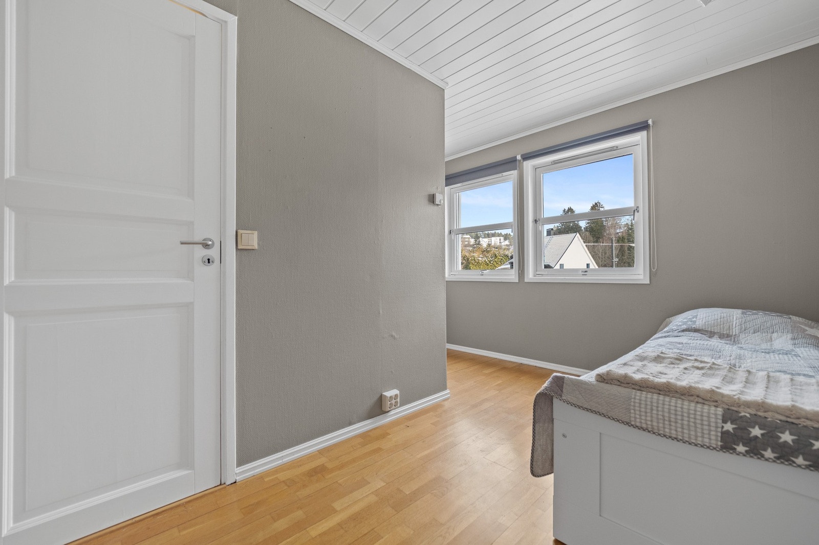 Soverommet har grå vegger, lyse gulv og to vinduer som gir godt med naturlig lys. Galleribilde