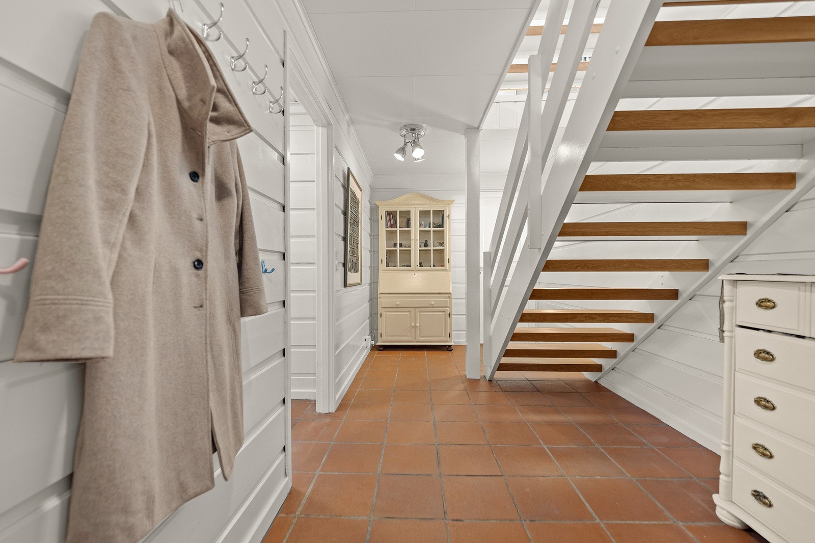 Lyst inngangsparti med flislagt gulv og trapp til andre etasje. Vegghengte knagger gir praktisk oppbevaring. Galleribilde