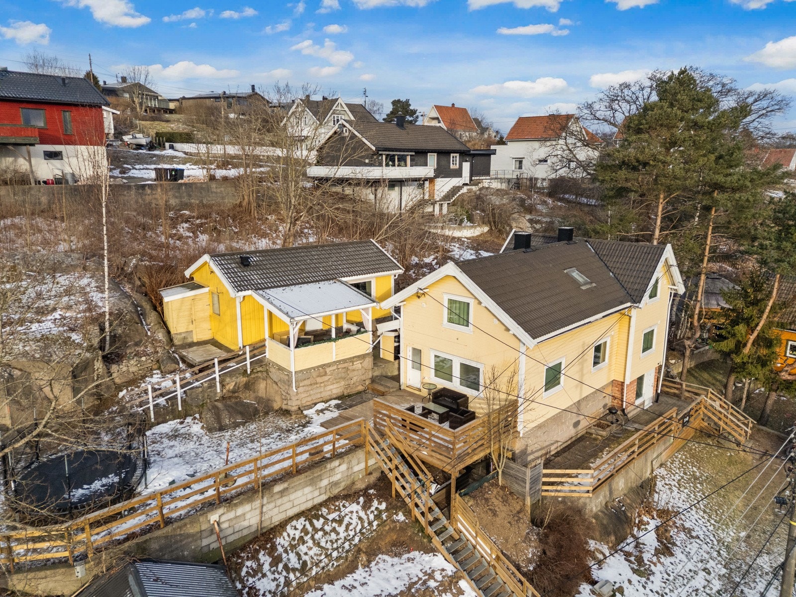 Eneboligen ligger på en skrånende tomt, opparbeidet med noe gressplen og diverse beplantning. Rett utenfor døra er det en bussholdeplass. Galleribilde