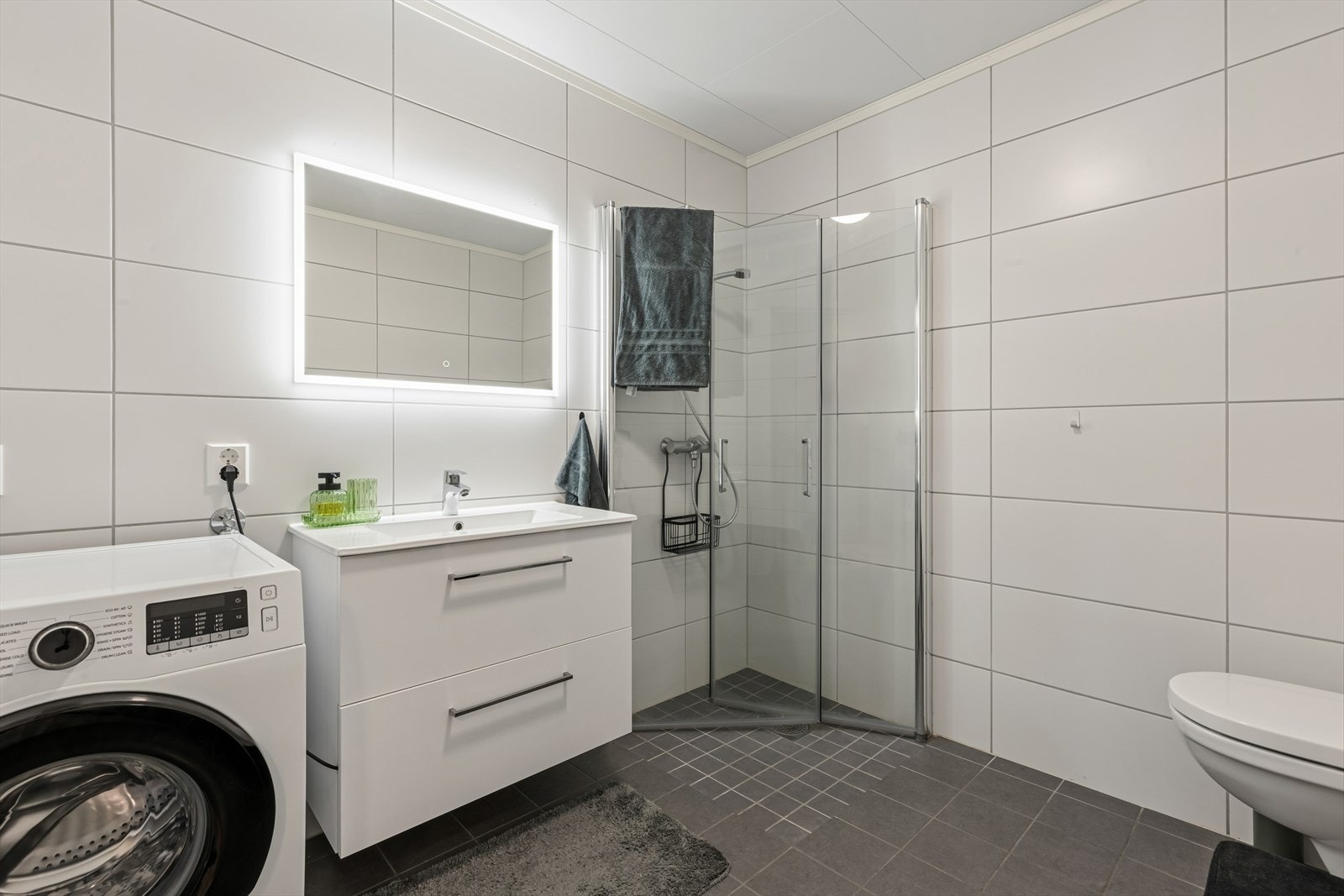 Badet er lyst og delikat. Badet er utstyrt med dusjhjørne, vegghengt wc og opplegg for både vaskemaskin og tørketrommel. Galleribilde