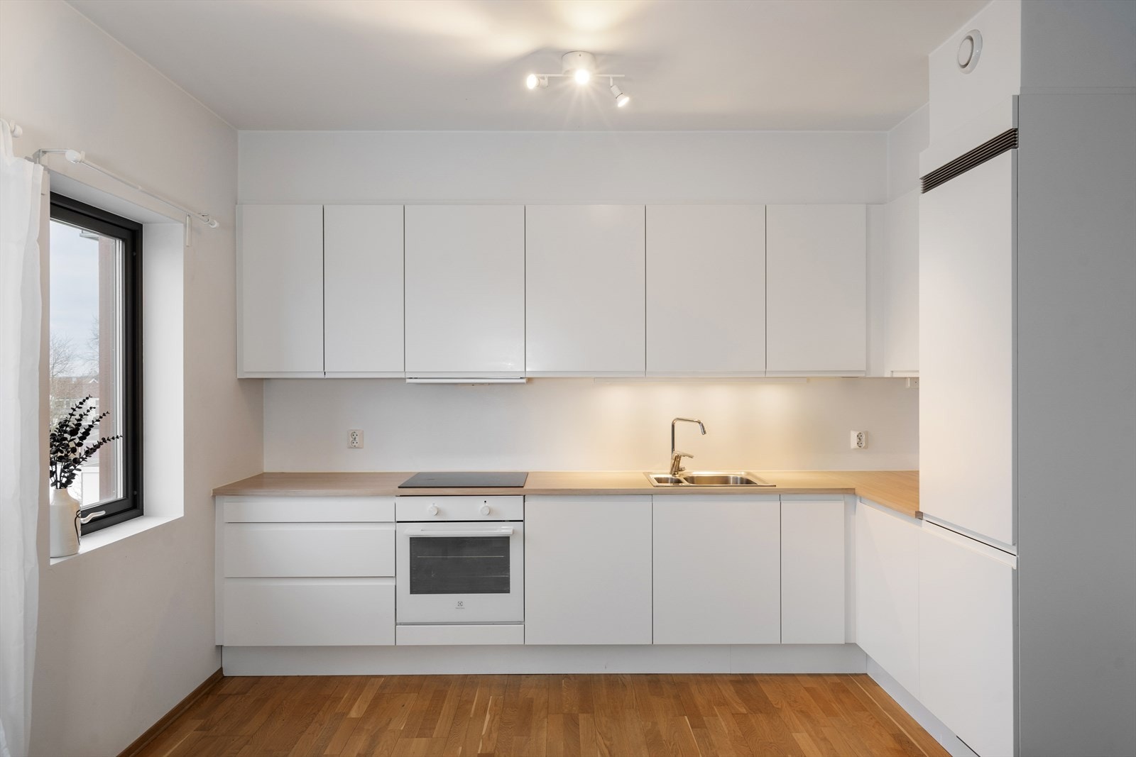 Lyst og tidløst kjøkken med platetopp, stekeovn, oppvaskmaskin og kjøl/frys integrert i innredningen Galleribilde