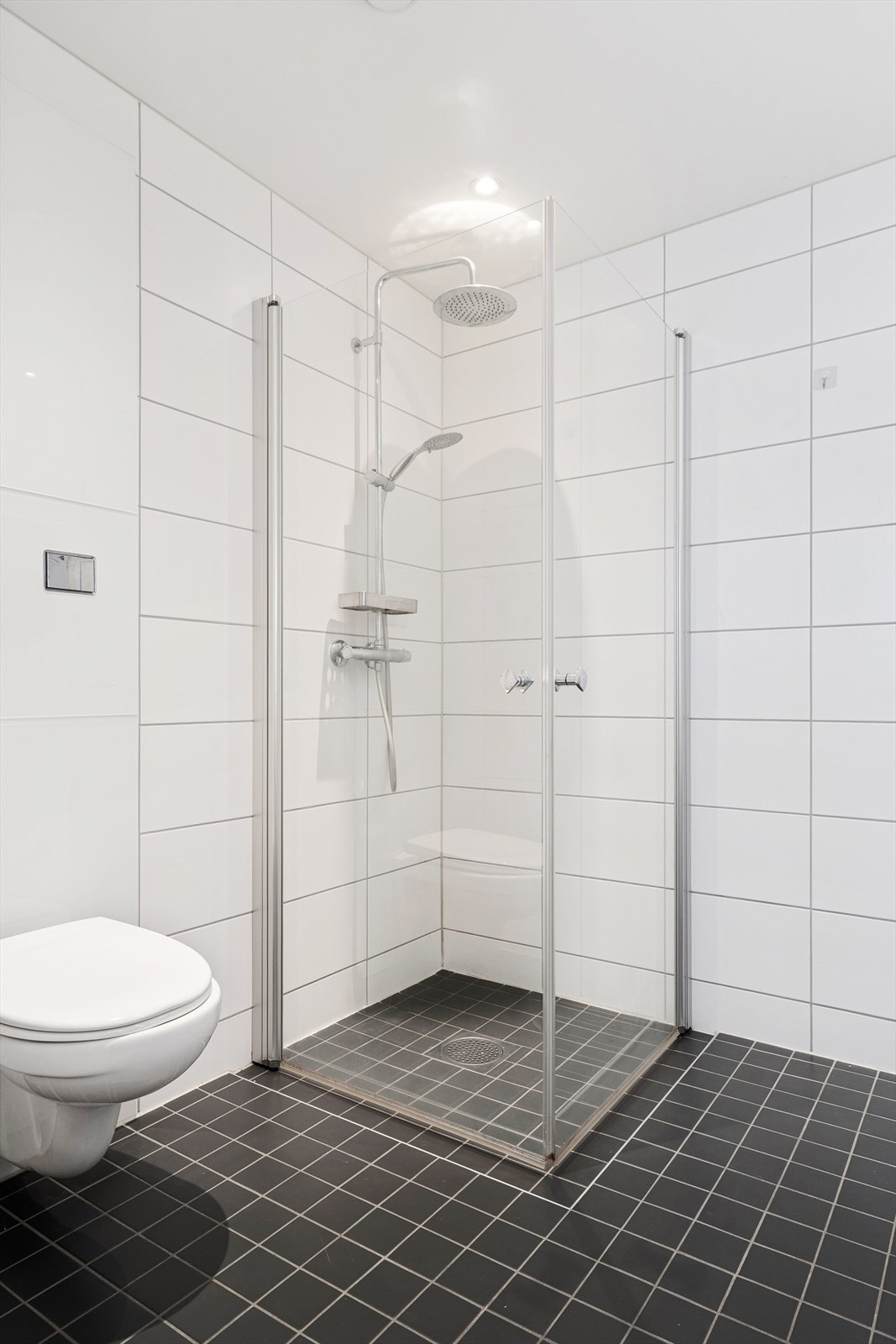 Baderomsinnredning bestående av benkeskap med glatte fronter, speil over servant, dusj med innfellbare dører i herdet glass, servant, veggfestet klosett med innebygget sisterne og opplegg for vaskemaskin/tørketrommel Galleribilde