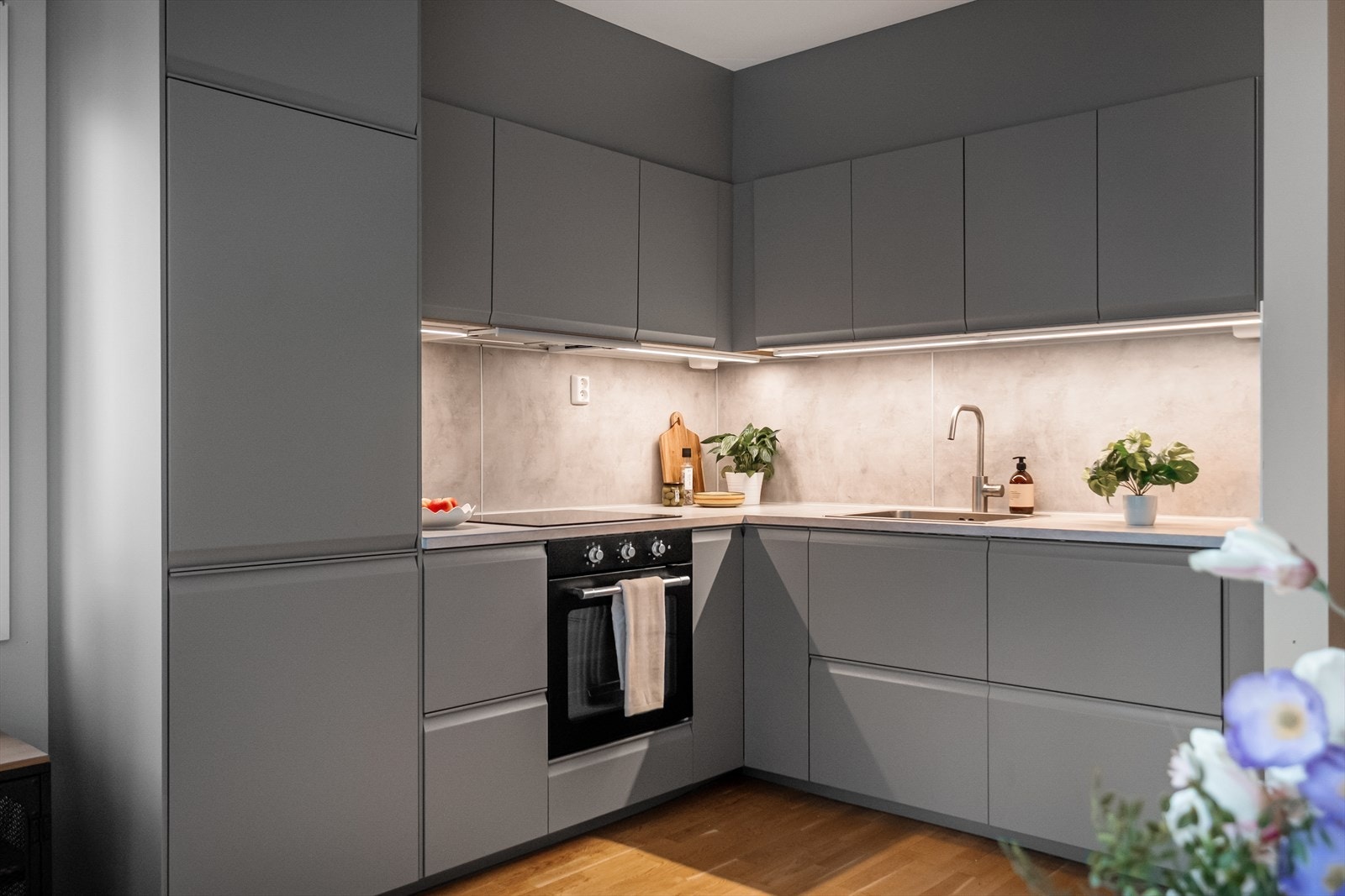 Moderne kjøkkeninnredning med glatte fronter, laminatbenkeplate med nedfelt vask og belysning over benkeplaten. Galleribilde