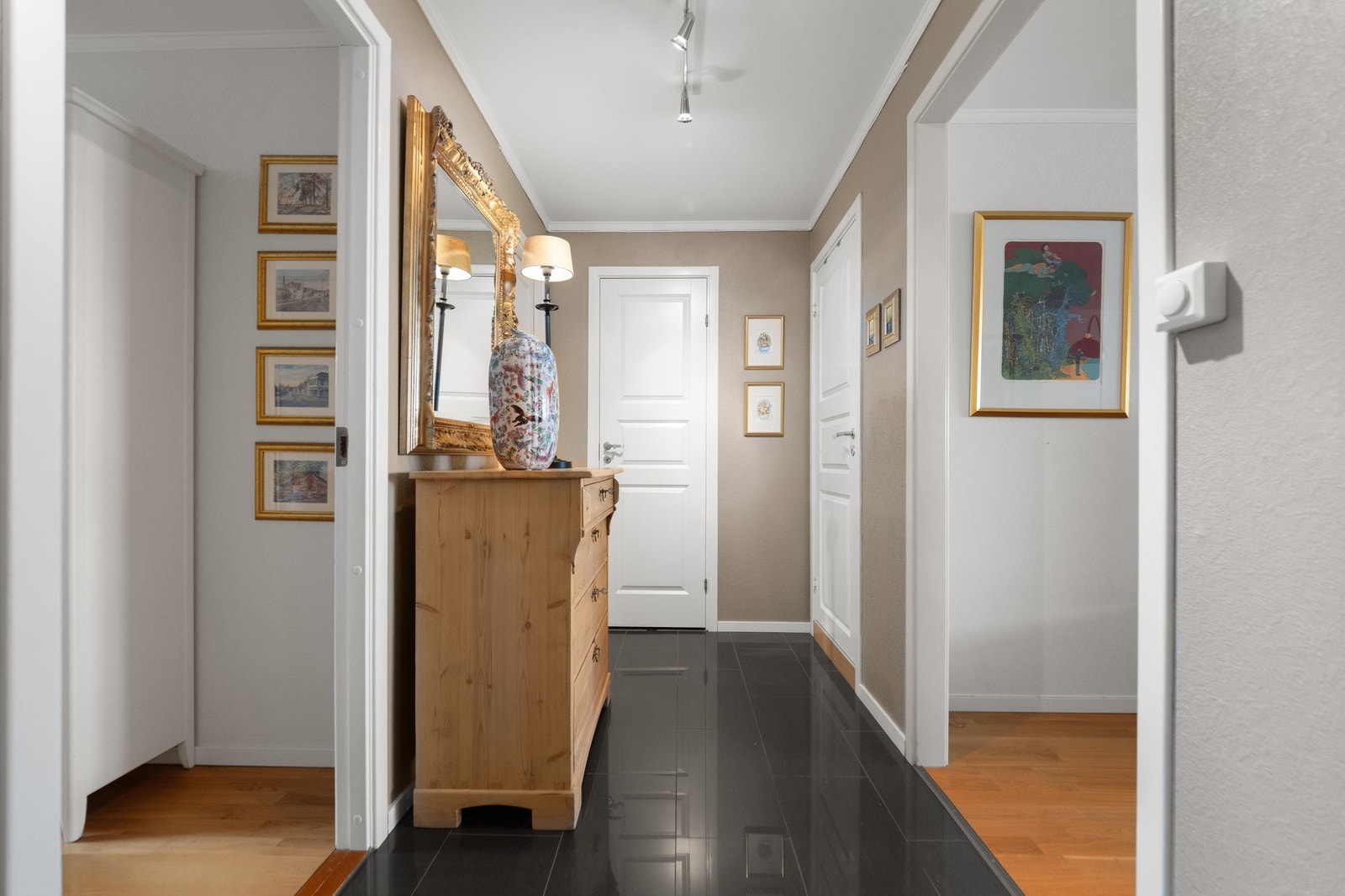 Gang med mørke fliser på gulv, lyse vegger og dører. Inngangsaprtiet har en elegant atmosfære. Galleribilde