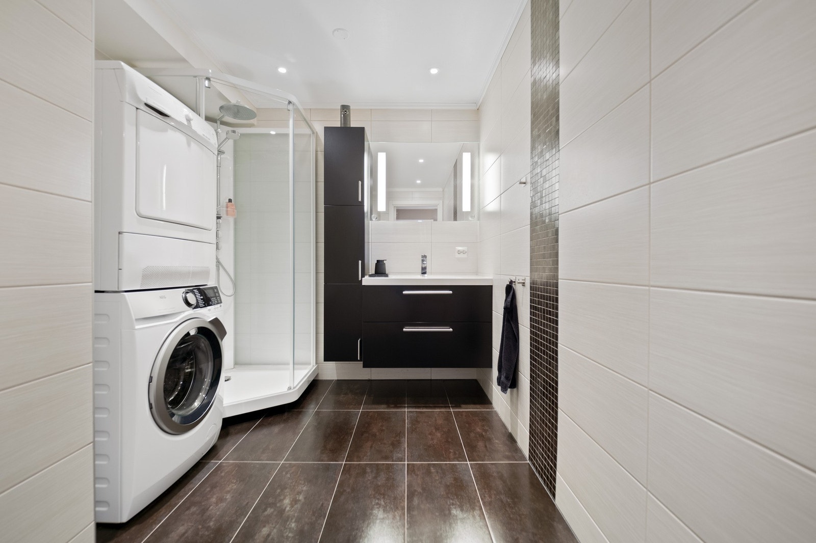 Moderne bad med dusjkabinett, vaskemaskin og tørketrommel, samt stilrene skap og belysning. Galleribilde