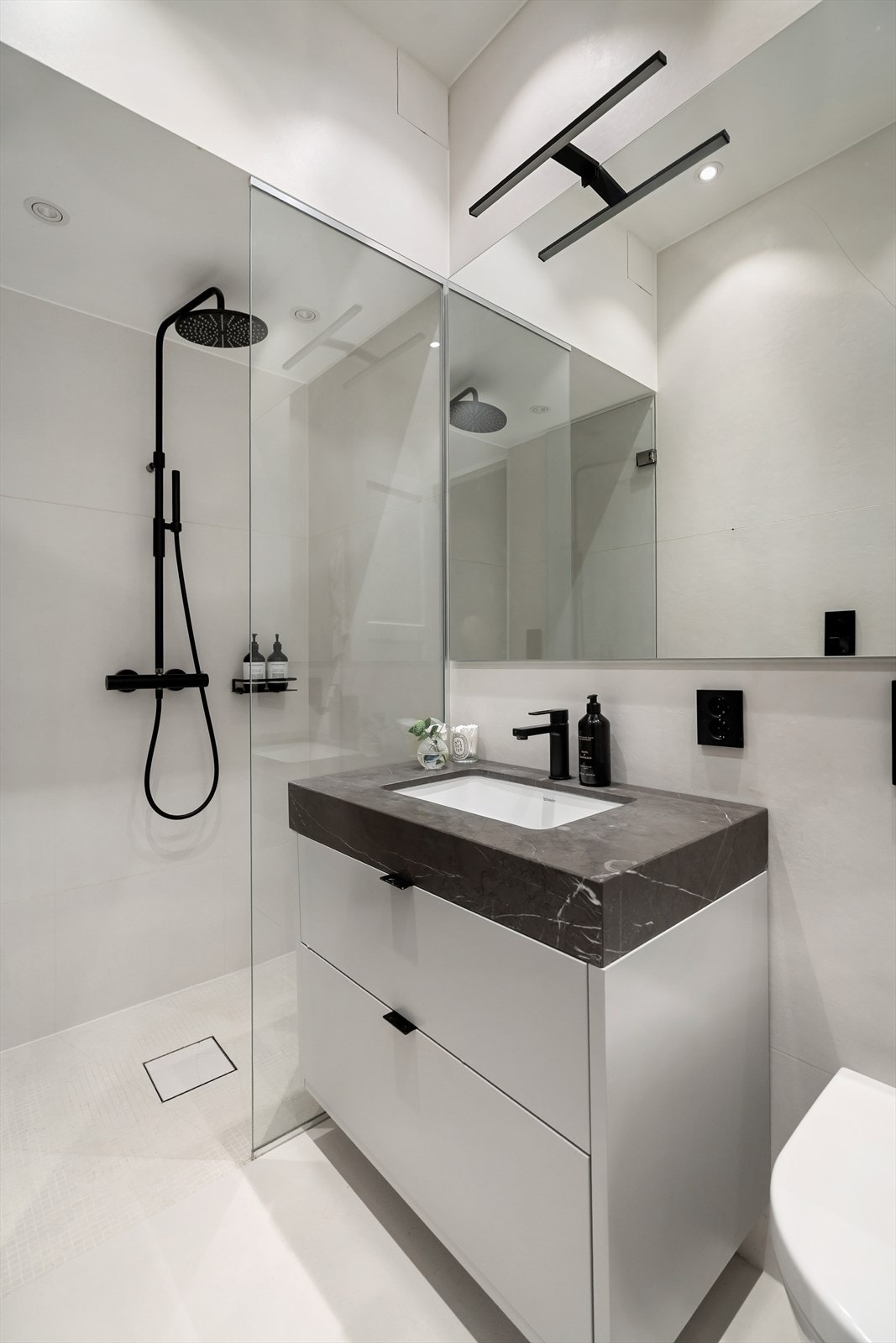 Bad 1 en-suite pusset opp i 2018, med dusjnisje med glassvegg, vegghengt toalett, spesialdesignet benkeplate i mørk marmor med servant, armatur fra Tapwell, fliser på 1,2 m x 1,2 m fra Bella Fliser & Design og varmekabler i gulv. Galleribilde