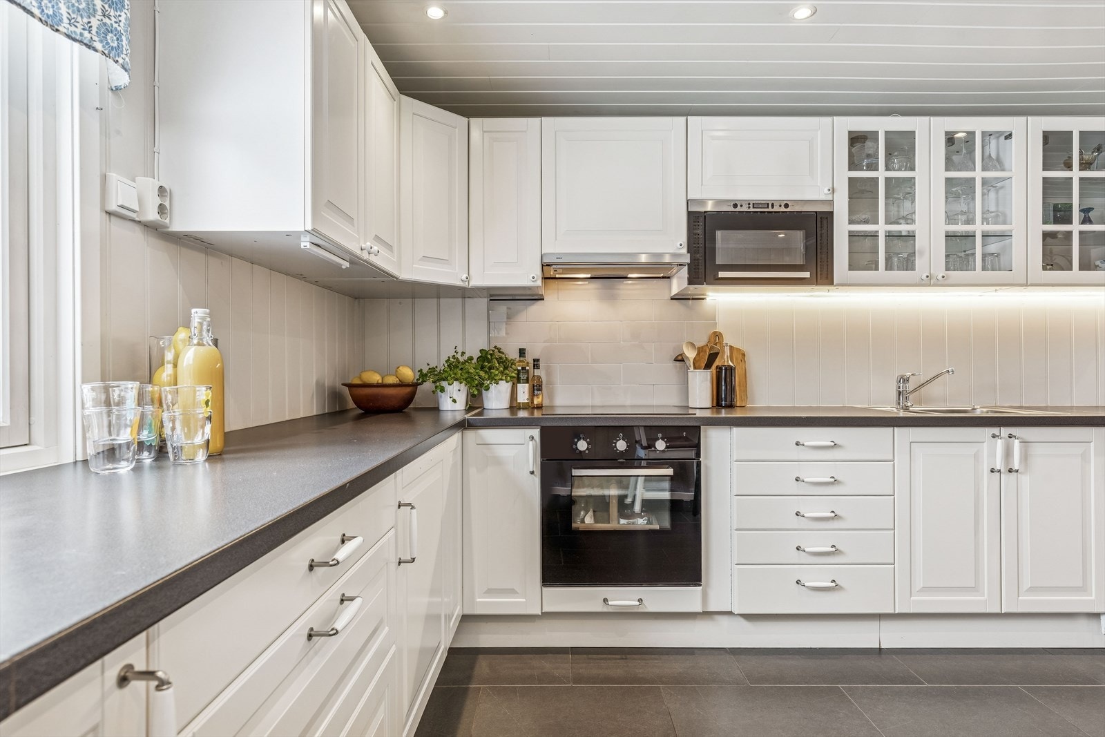 Kjøkkeninnredningen har profilerte fronter, fire overskap med glassdører og Lindas dekorflis ved platetopp. Galleribilde